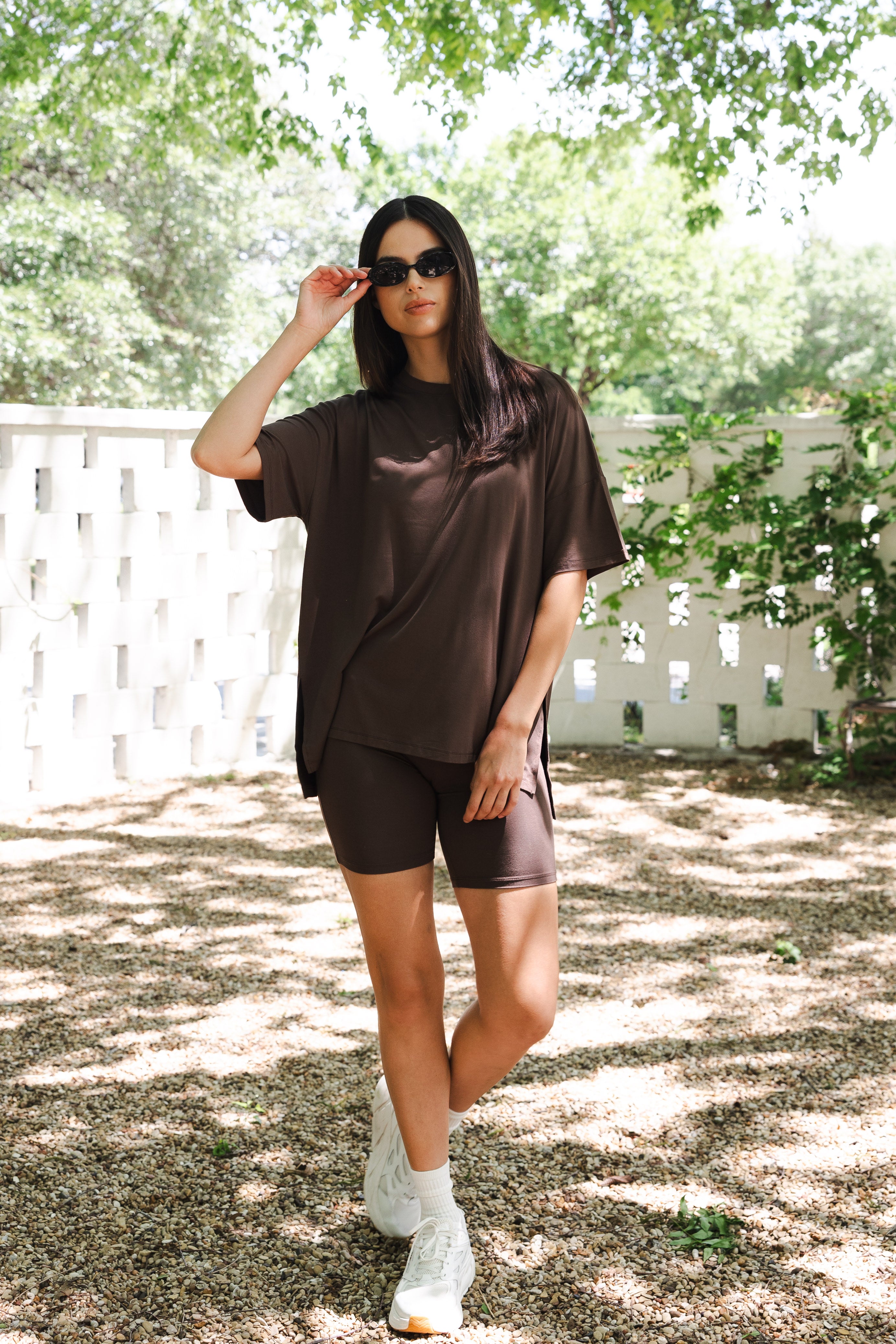 Female posing outside in front of a white fence wearing the Women’s Biker Short Set in Espresso