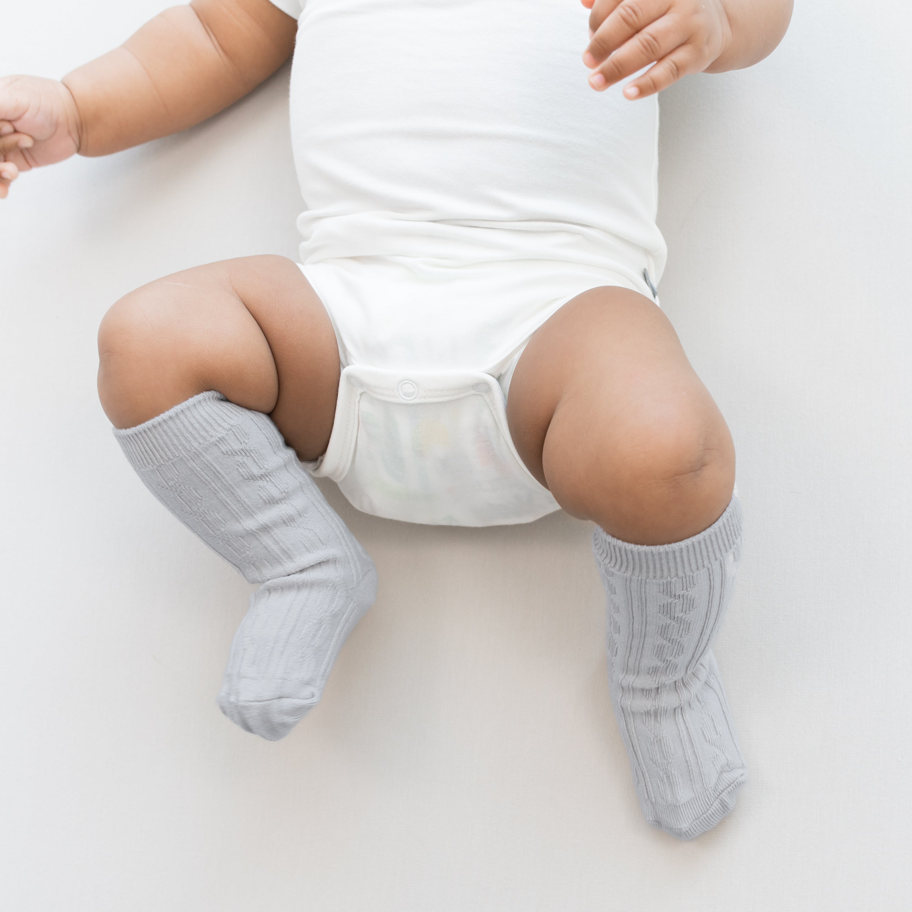 Close up of infant wearing the Knee High Socks in Storm paired with a Cloud bodysuit on a light neutral background