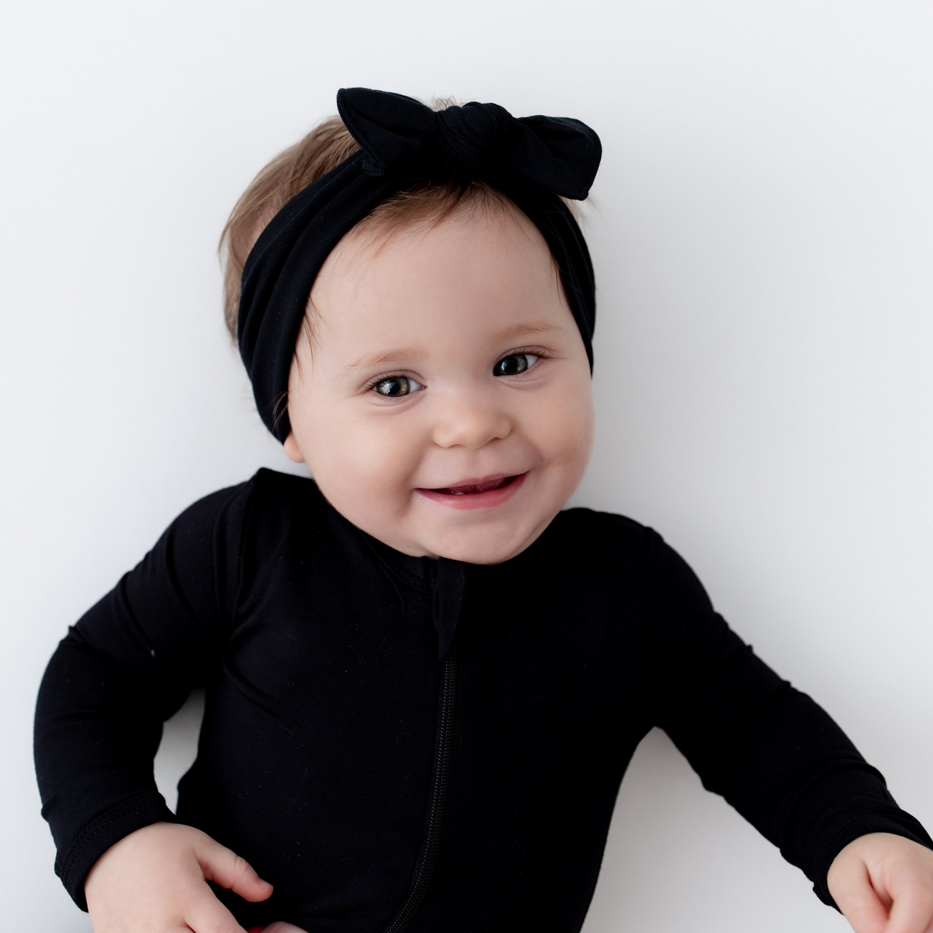 Smiling baby wearing Knotted Bow Headband in Midnight and matching zippered footie