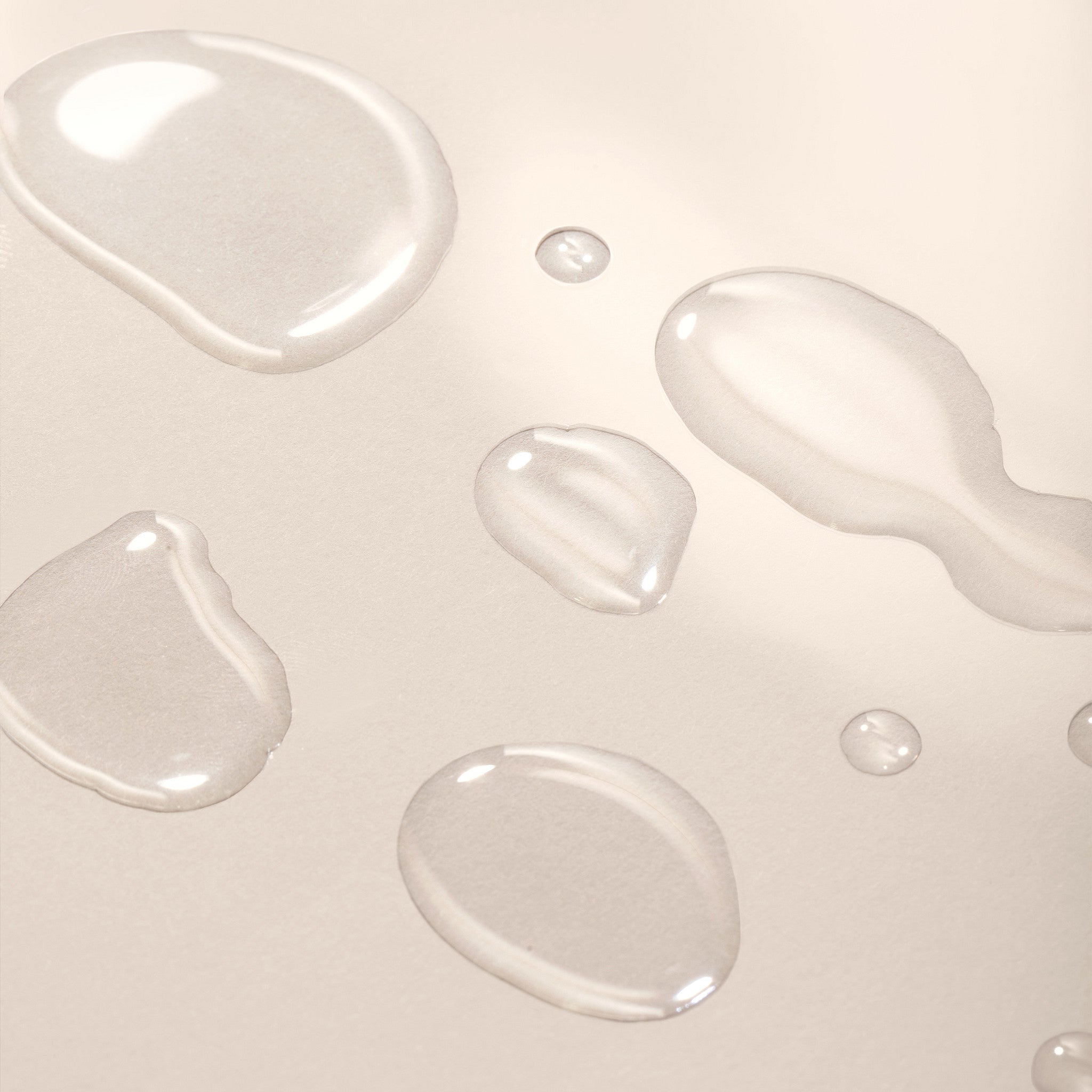 Close-up of clear liquid droplets on a light beige background