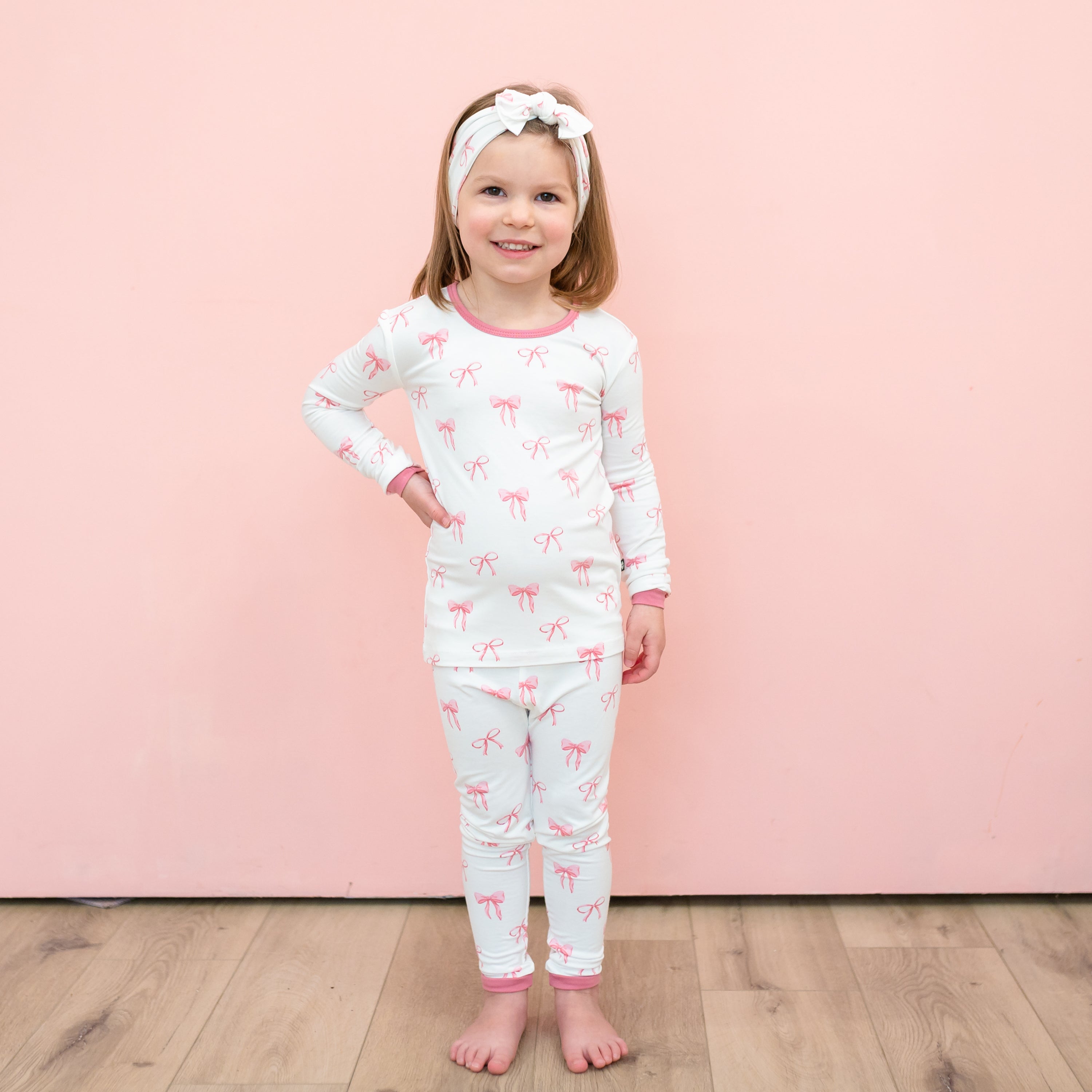 Toddler modeling Long Sleeve Pajamas in Bow with matching headband