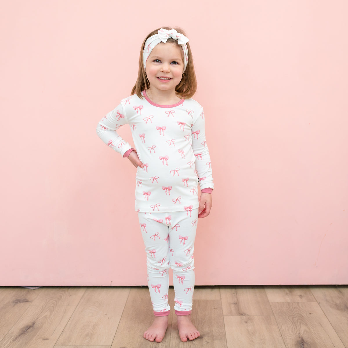 Toddler modeling Long Sleeve Pajamas in Bow with matching headband