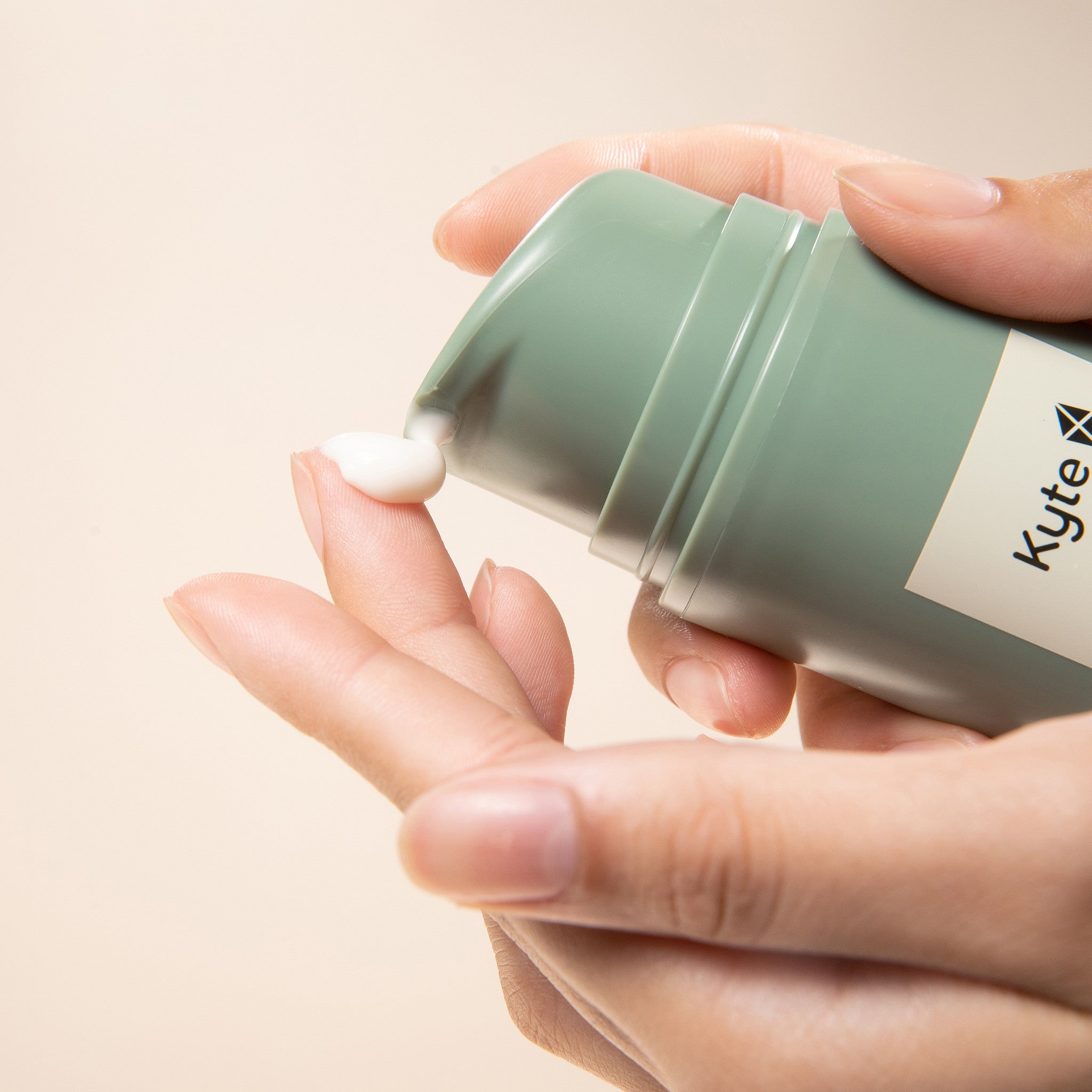 Hand holding a green container of Kyte skincare eczema cream with a beige background