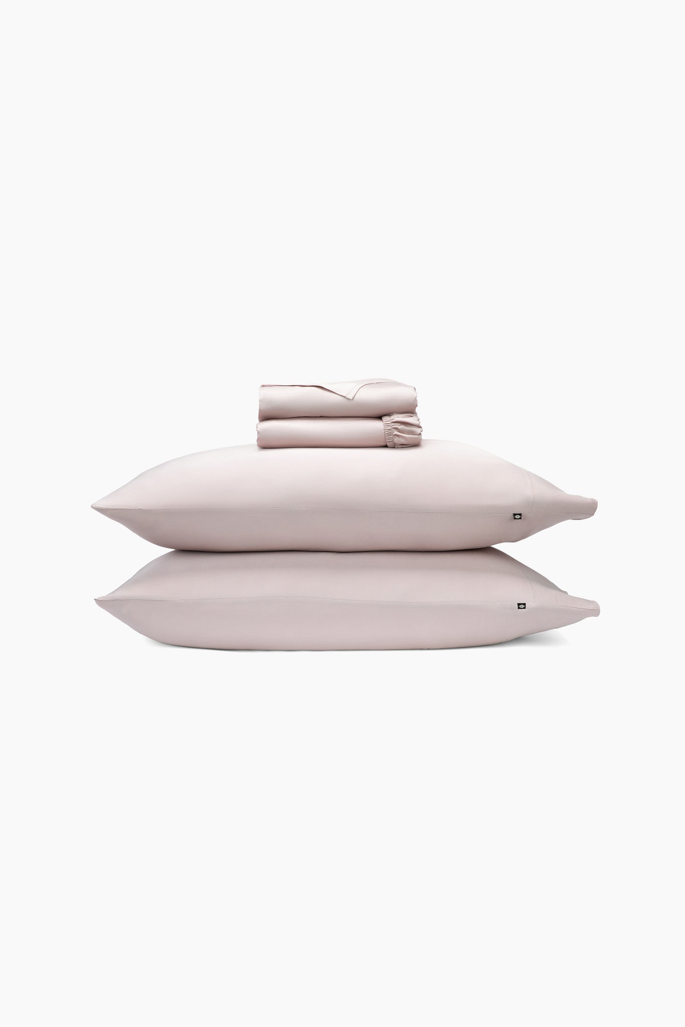 Set of light pink bedding including two pillows and a folded sheets on a white background