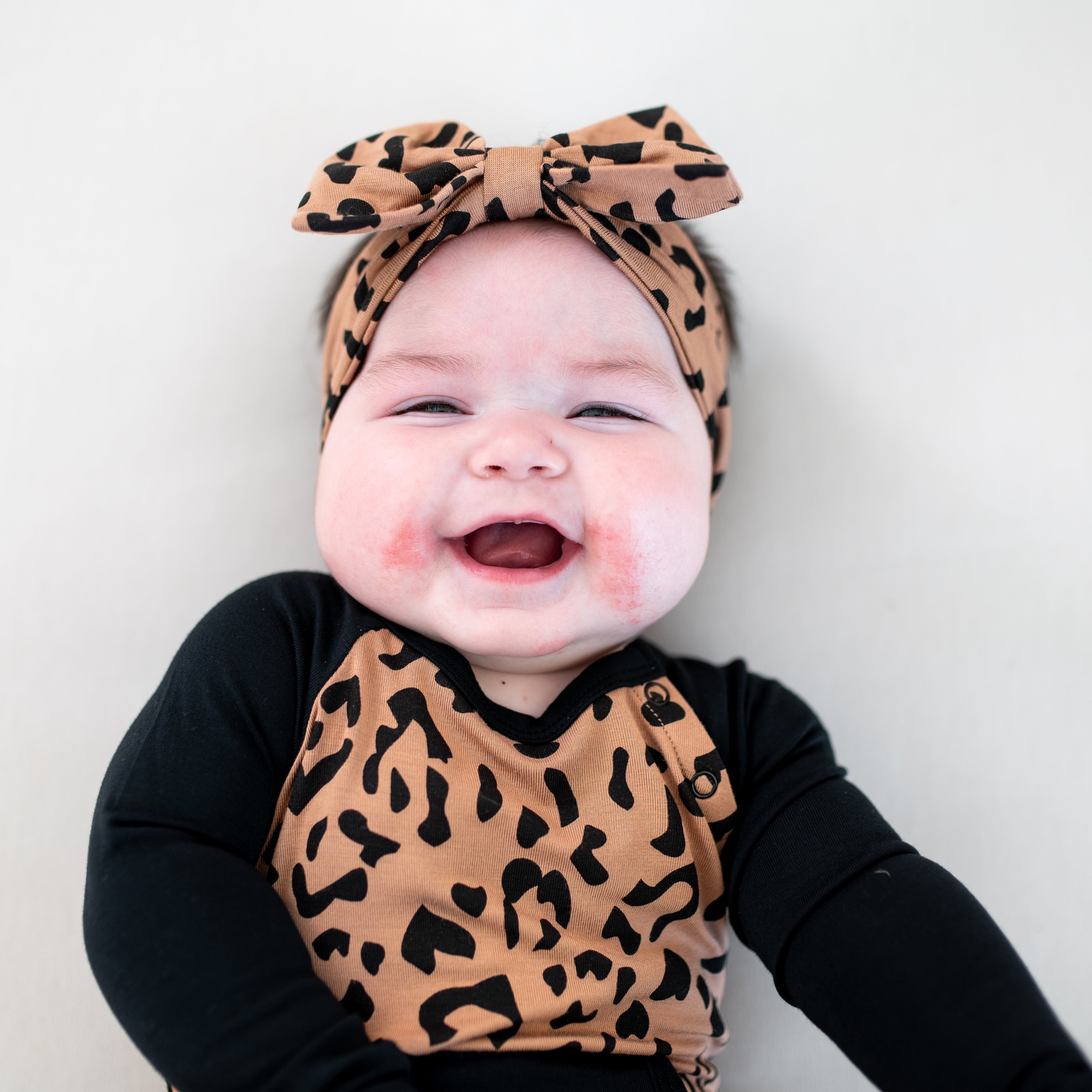 Close up of the Longall in Latte Leopard on a smiling infant showing the top snap closure and Midnight accent on the shoulders and arms