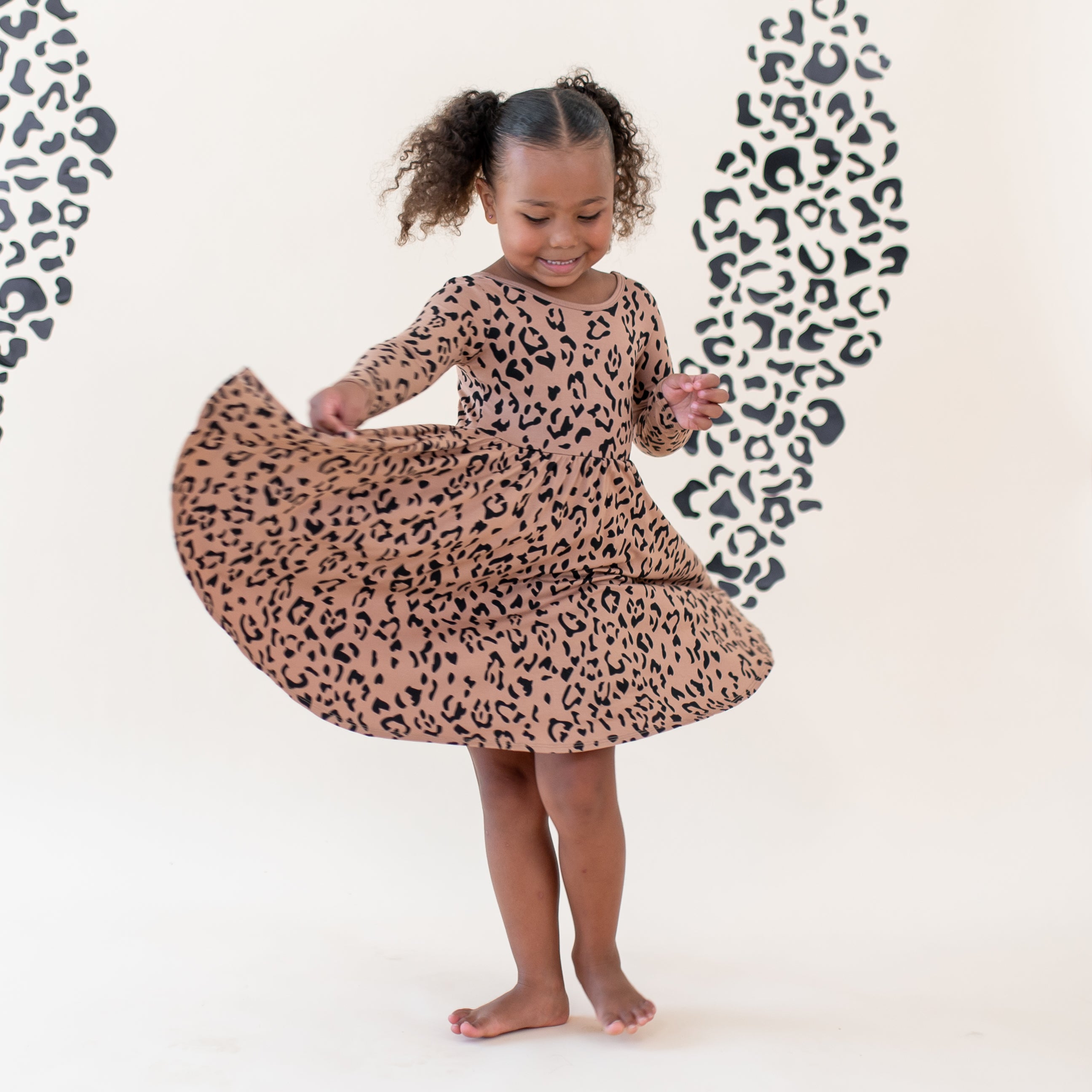 Girl twirling in her Long Sleeve Twirl Dress in Latte Leopard in front of a light colored leopard print backdrop