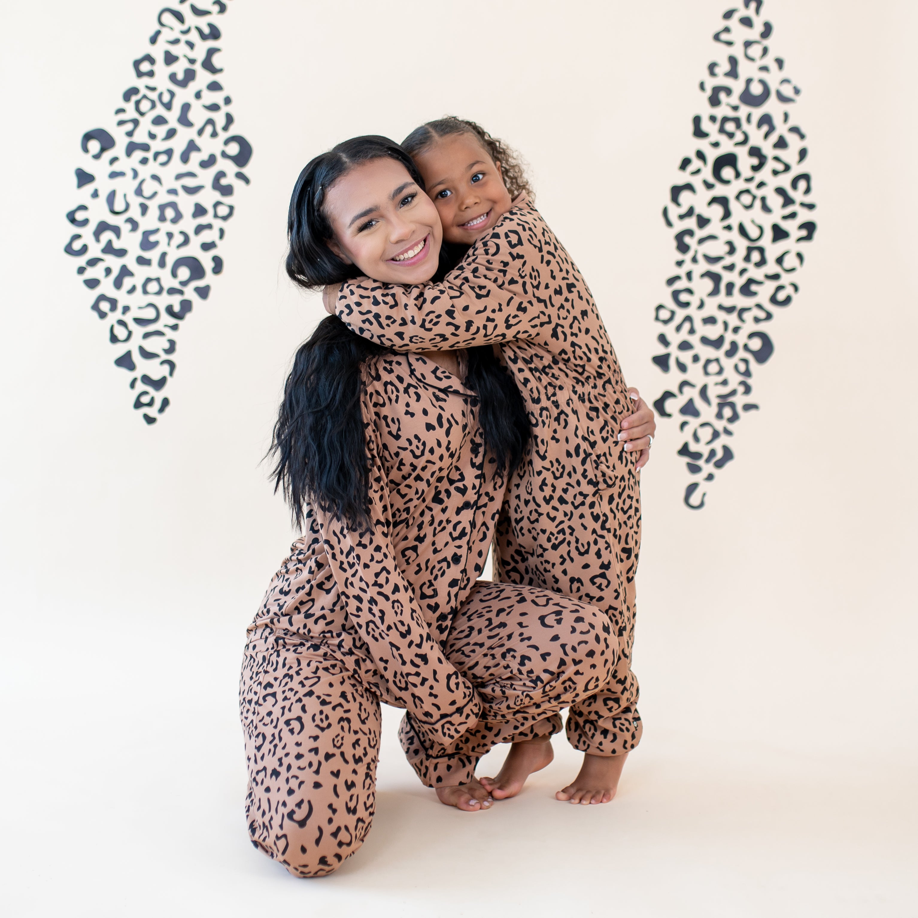 Mother kneeling on the ground hugging her daughter matching in Latte Leopard pajamas