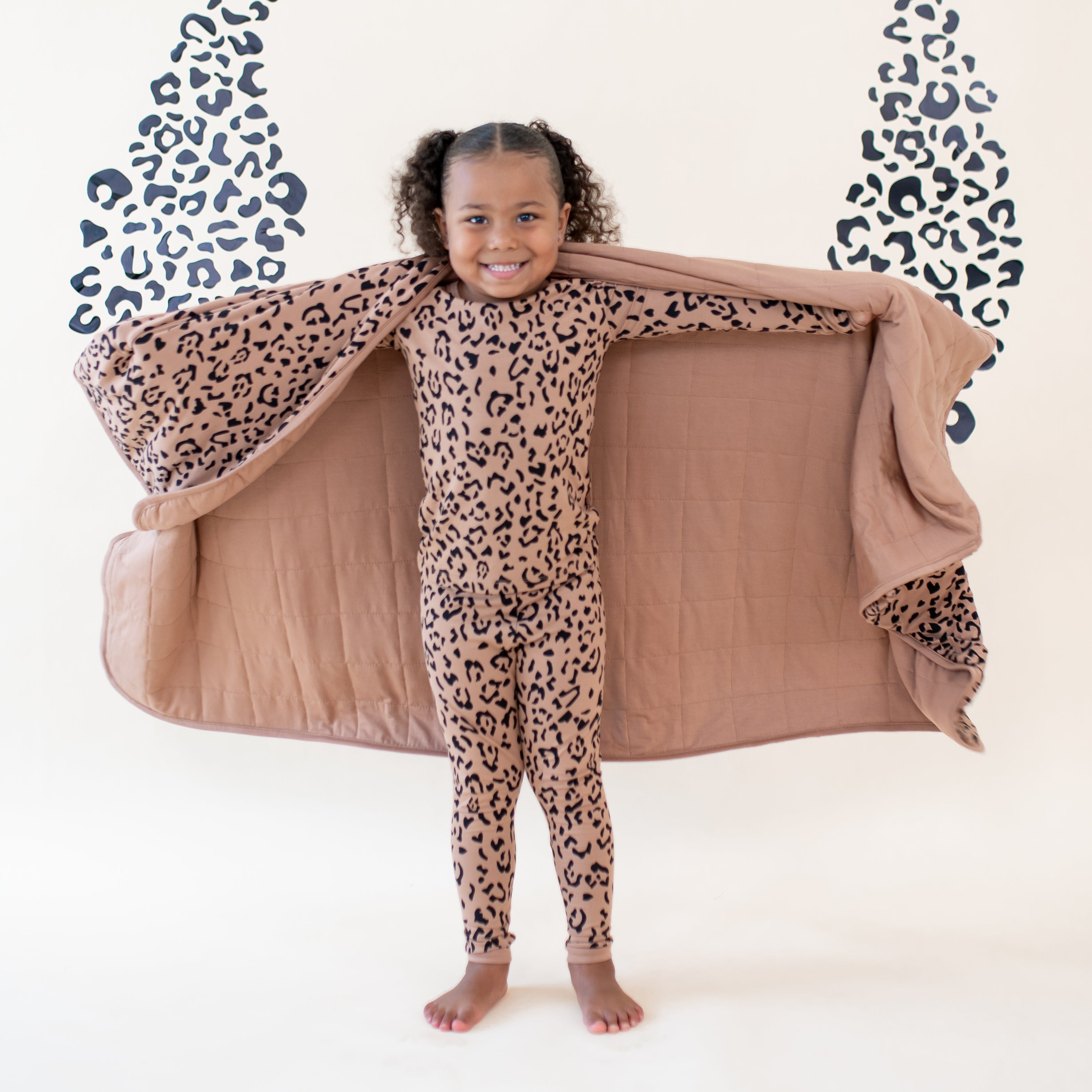 Young girl with the Toddler Blanket in Latte Leopard 1.0 around her shoulders showing the latte backing wearing latte leopard long sleeve toddler pajamas