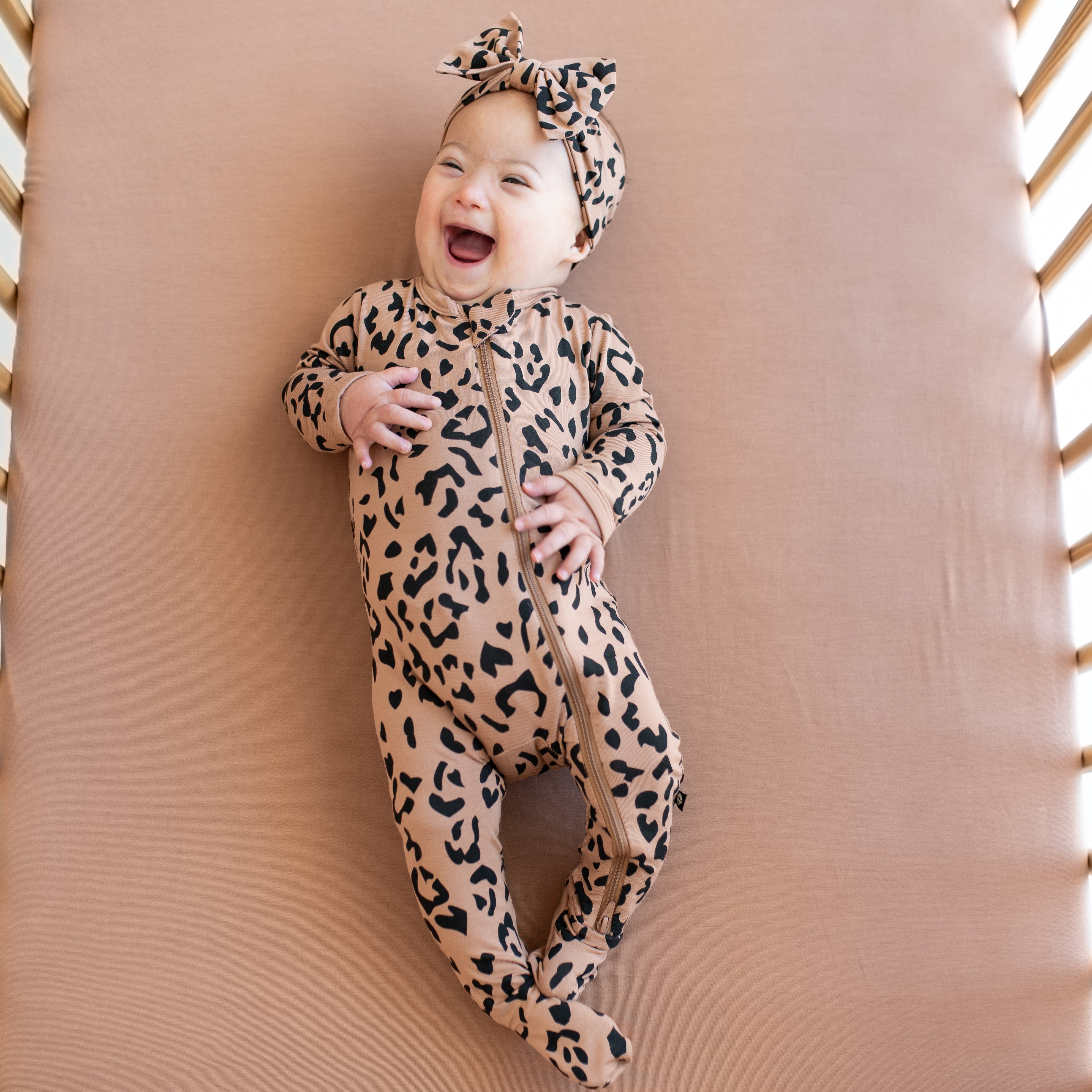 Baby wearing Zippered Footie in Latte Leopard with matching bow headband