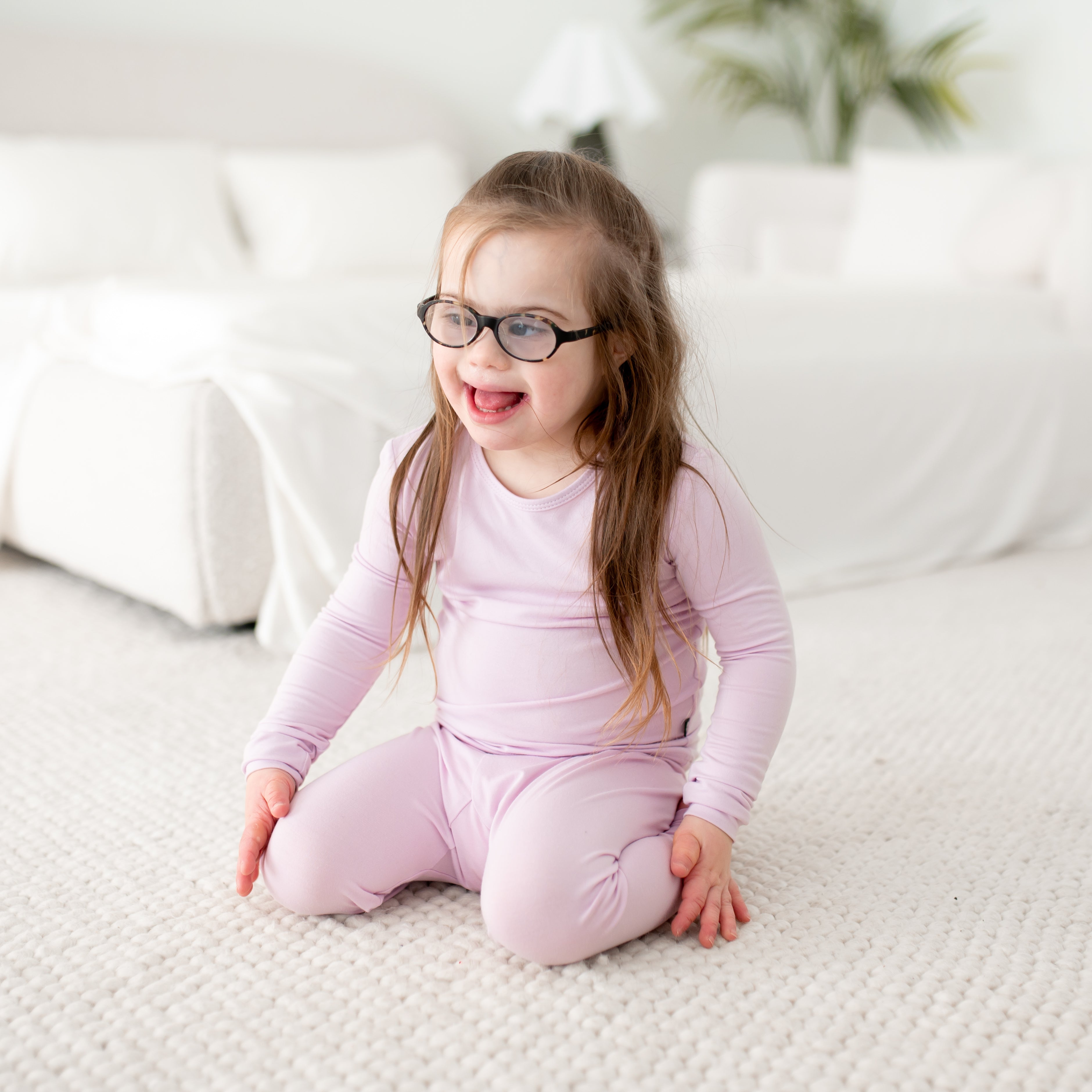 Child wearing glasses and a purple pajama sitting on a white couch.