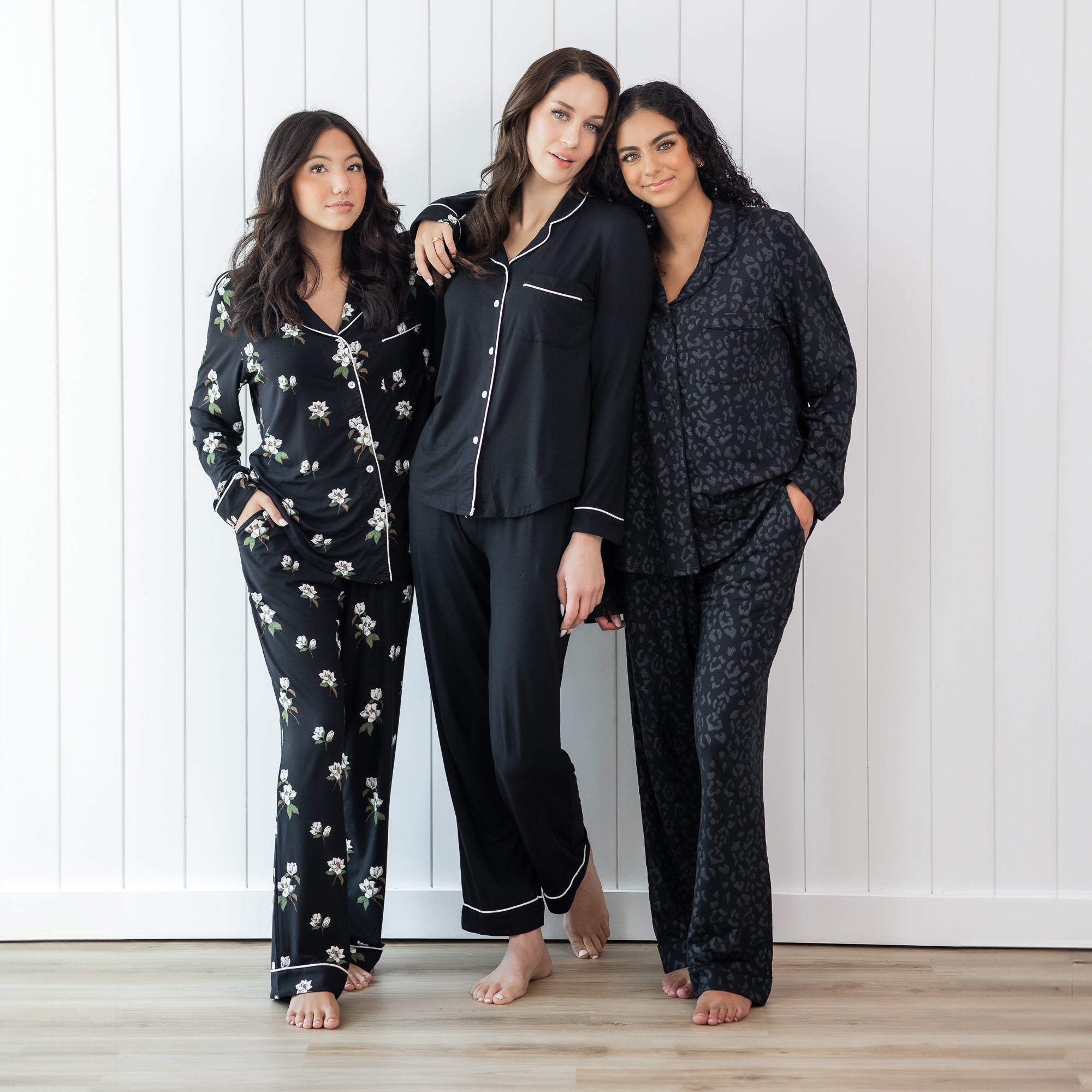 Three females standing side by side wearing the Long-Sleeved Women's Pajama Set in Midnight Leopard, Midnight with cloud trim and Big Magnolia in Midnight