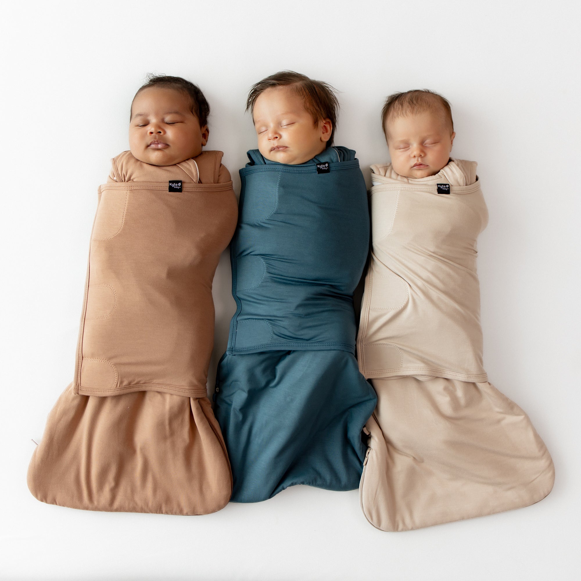 Sleeping babies laying side by side wearing the sleep bag swaddlers in Latte, Atlantic and Bisque