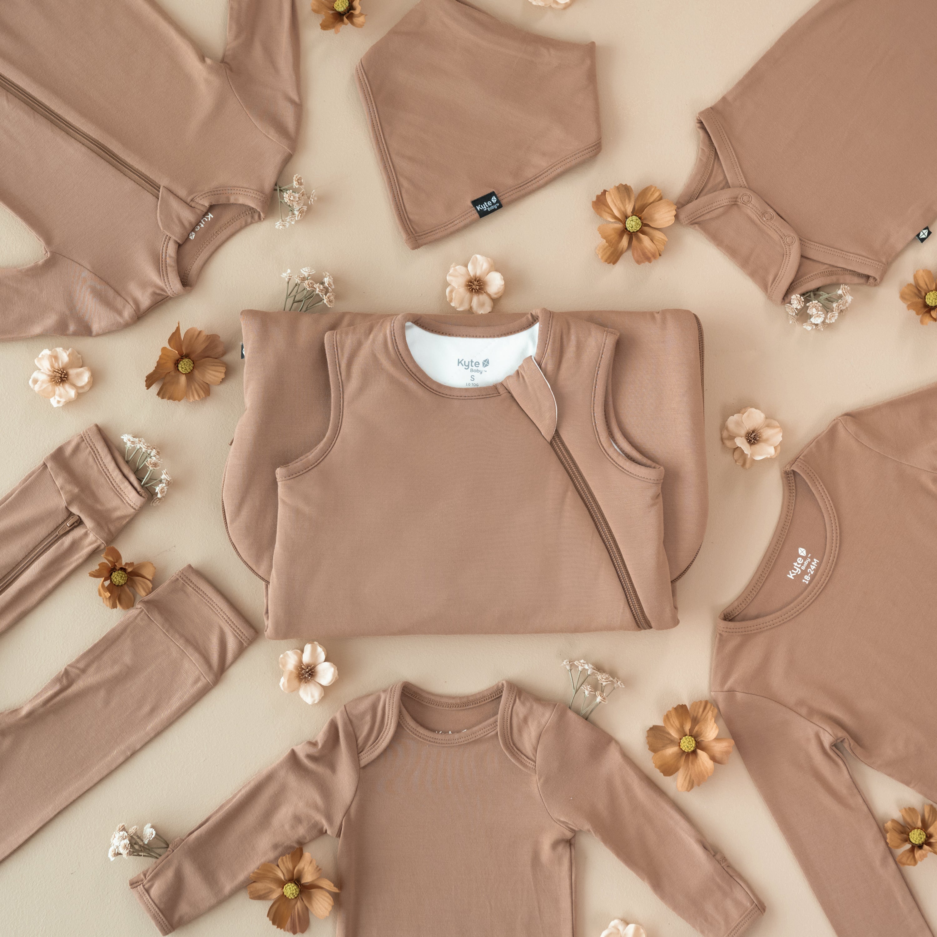 Fat Lay of Latte items. Sleep bag in the middle surrounded by long sleeve bodysuits, long sleeve toddler pajama and a bib