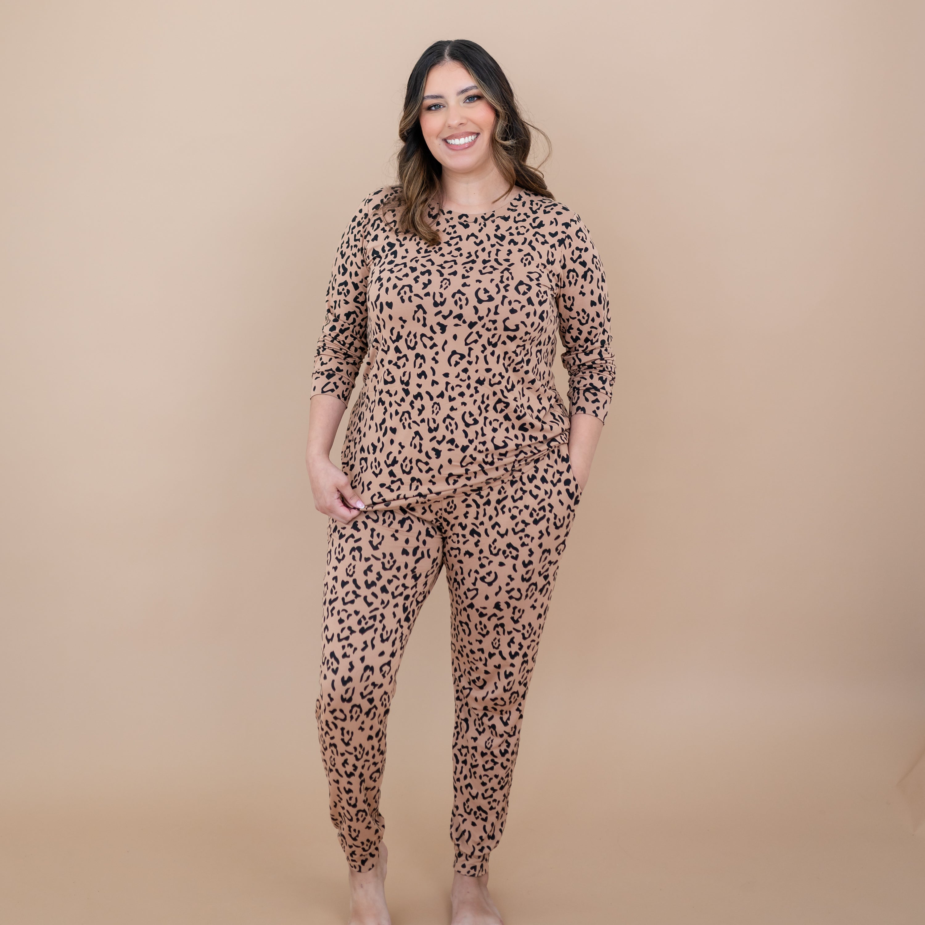 Smiling female standing with one hand in the pants pocket of the Women's Jogger Pajama Set in Latte Leopard in front of a taupe backdrop