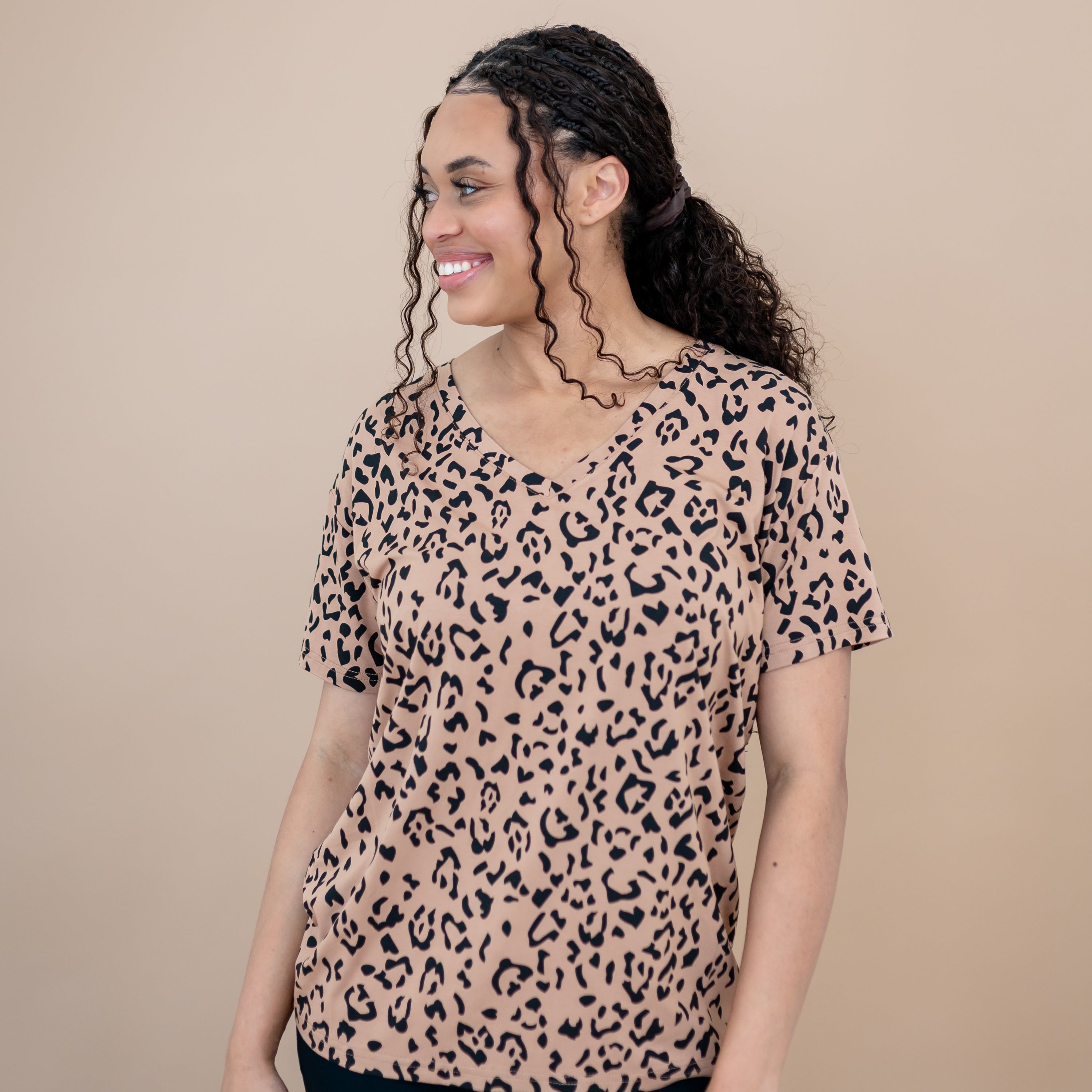 Smiling female model looking off to the side wearing the Women's Relaxed Fit V-Neck in Latte Leopard standing in front of a taupe backdrop