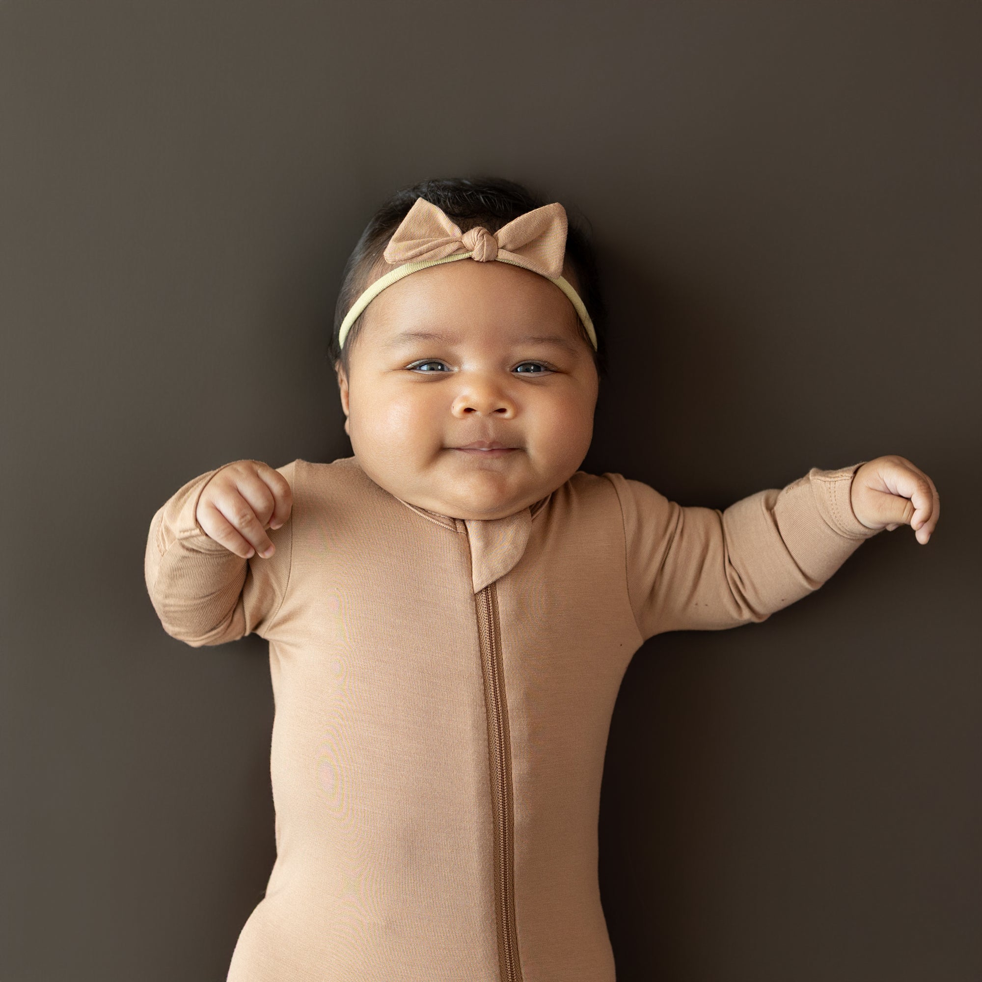 Infant wearing the Tiny Nylon Bow in Latte with matching zippered footie