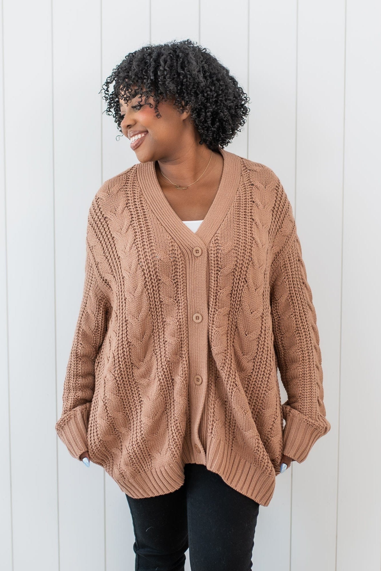 Female model wearing the Cable Knit Adult Cardigan in Latte buttoned up paired with black pants