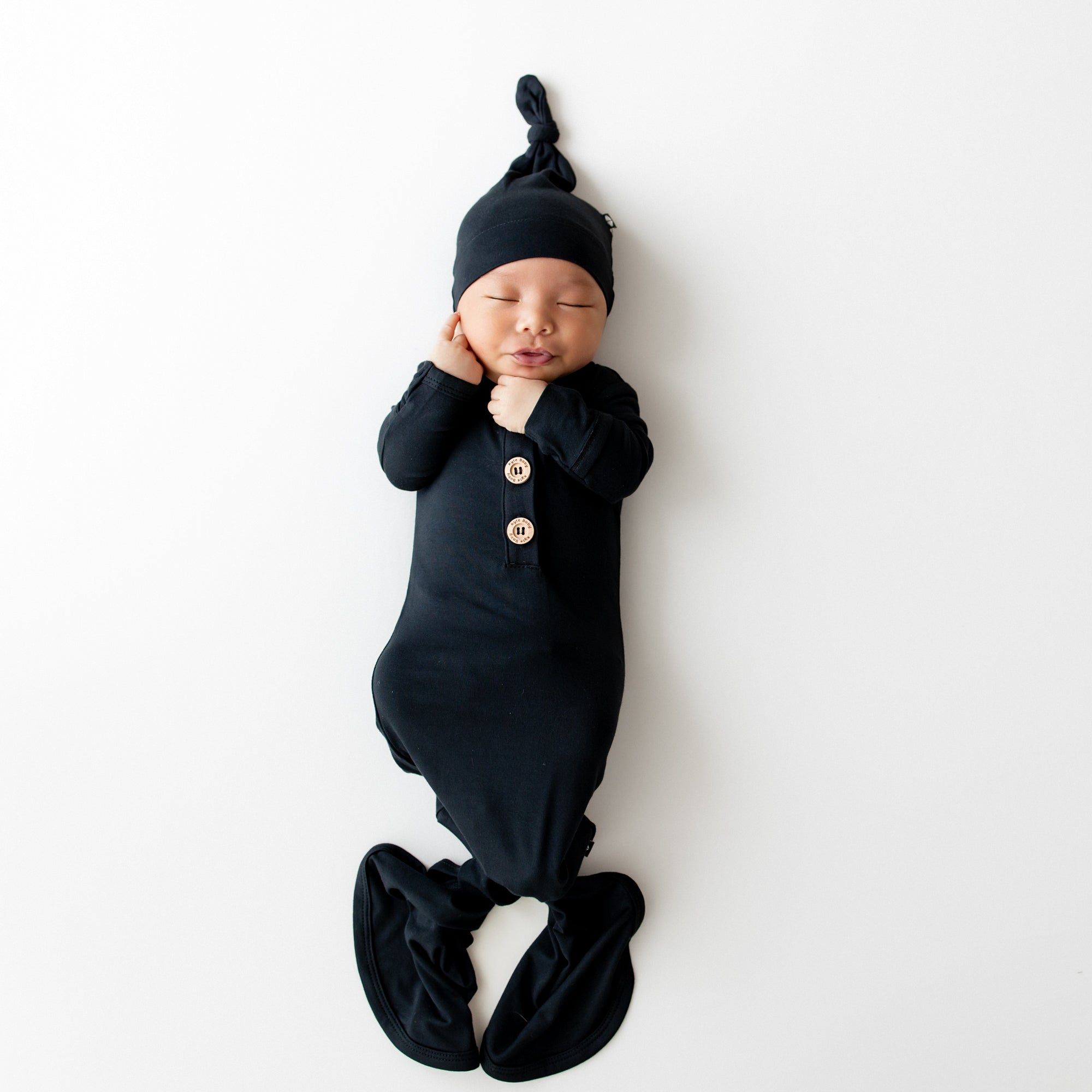 Newborn baby wrapped in a black outfit with buttons and a matching hat on a white background