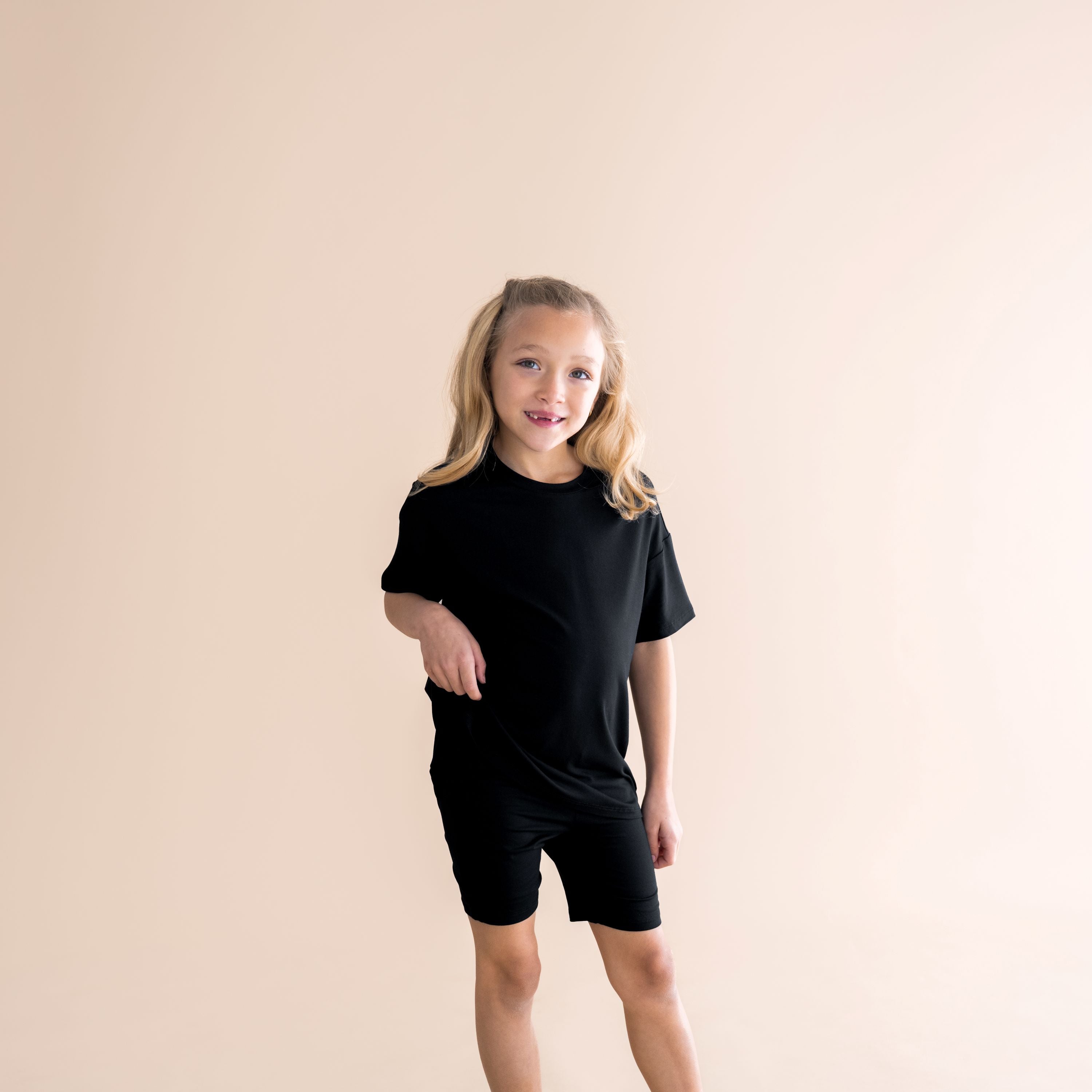 Young girl posing wearing the Toddler Biker Short Set in Midnight in front of a light taupe background