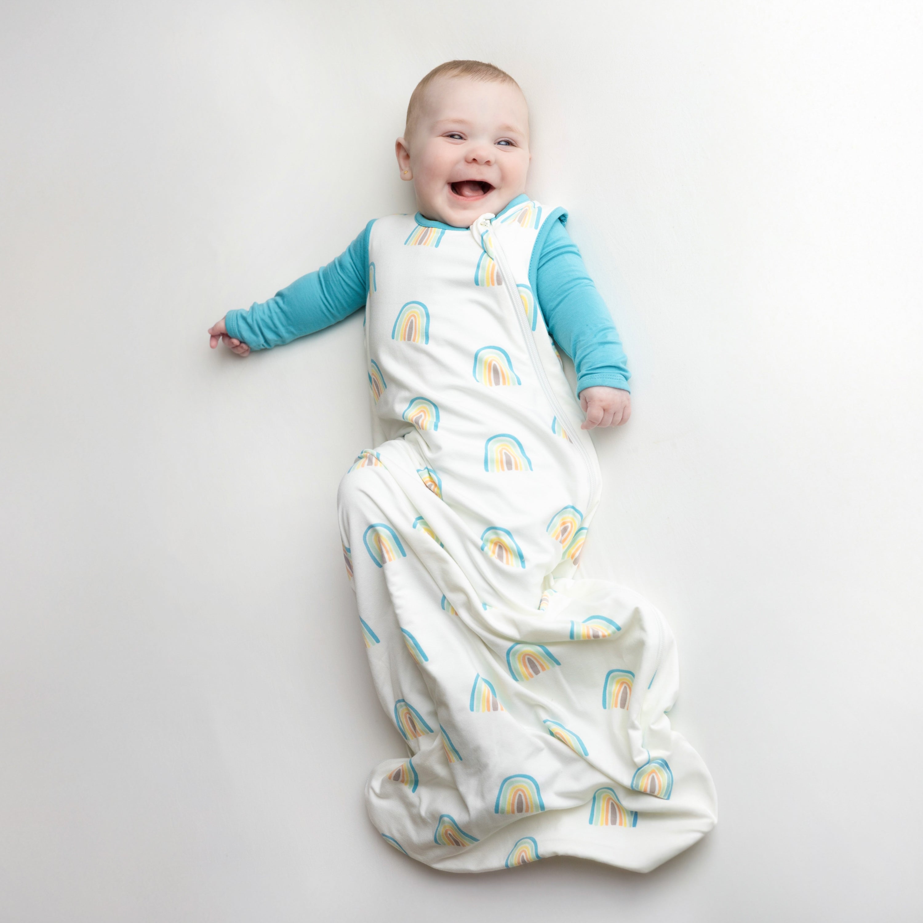 Smiling baby wearing a Makai Romper underneath the Sleep Bag in Makai Rainbow 0.5