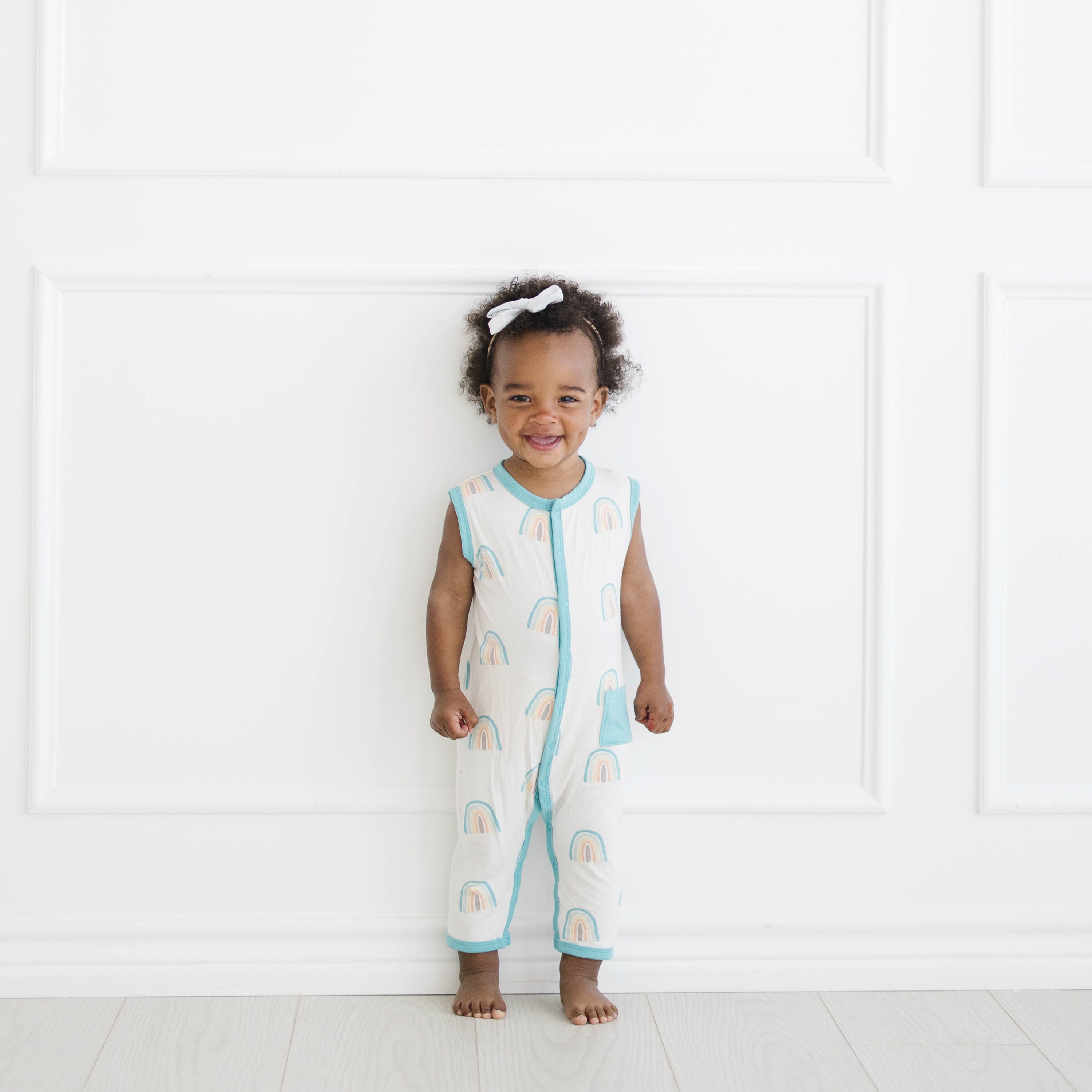 Toddler wearing Sleeveless Snap Romper in Makai Rainbow with White Bow