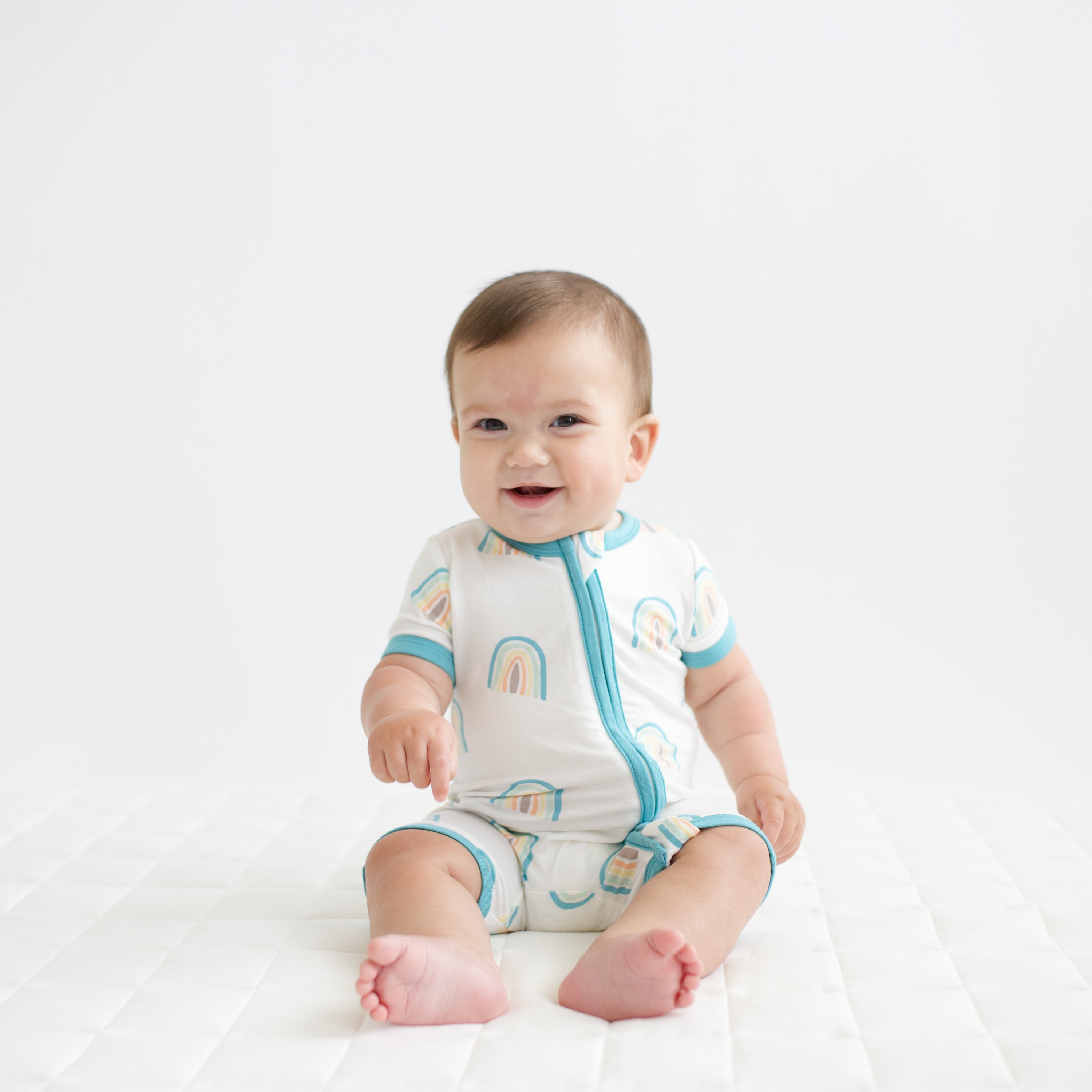 Infant wearing Kyte Baby Zippered Shortall Romper with dual zipper in Makai Rainbow