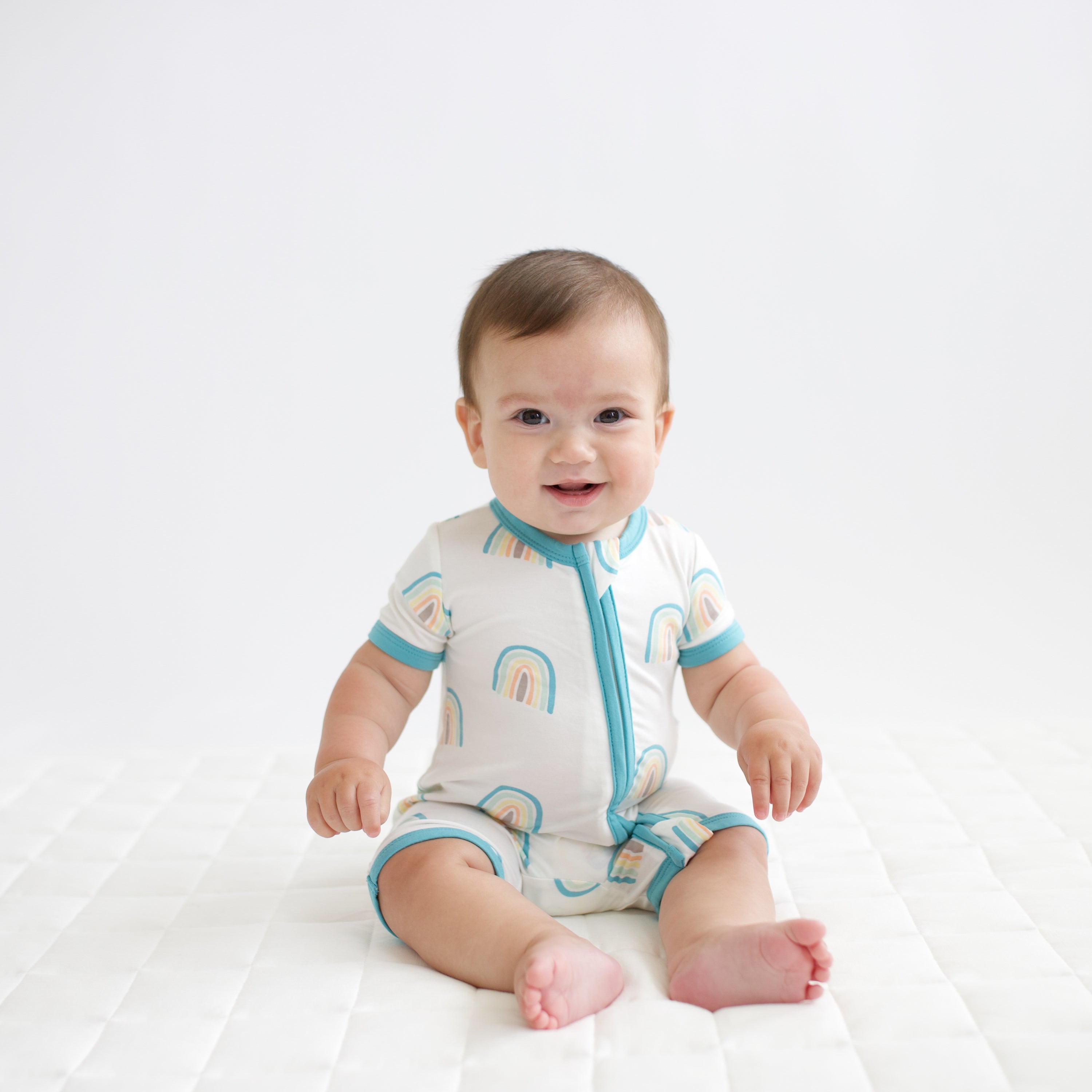 Infant wearing Kyte Baby Zippered Shortall Romper in Makai Rainbow