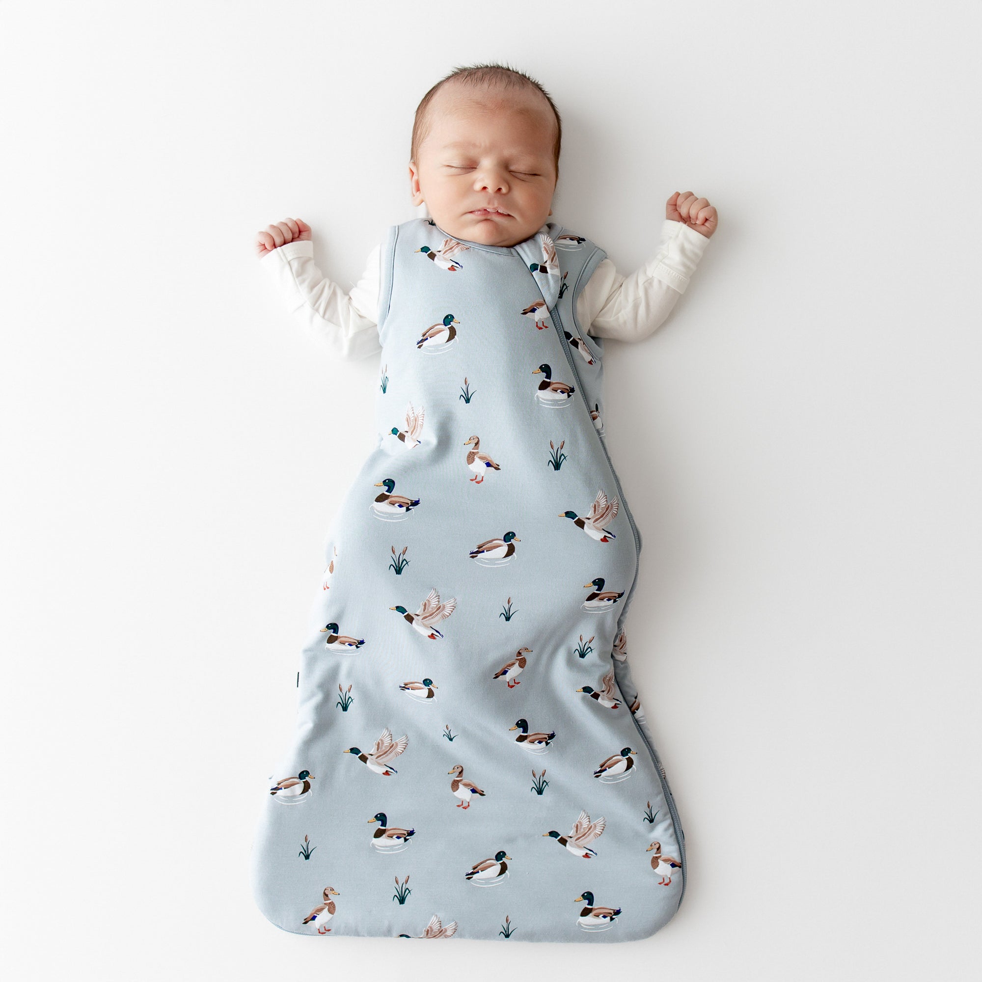 Sleeping newborn wearing the Sleep Bag in Mallard Duck 1.0 with a white romper on underneath