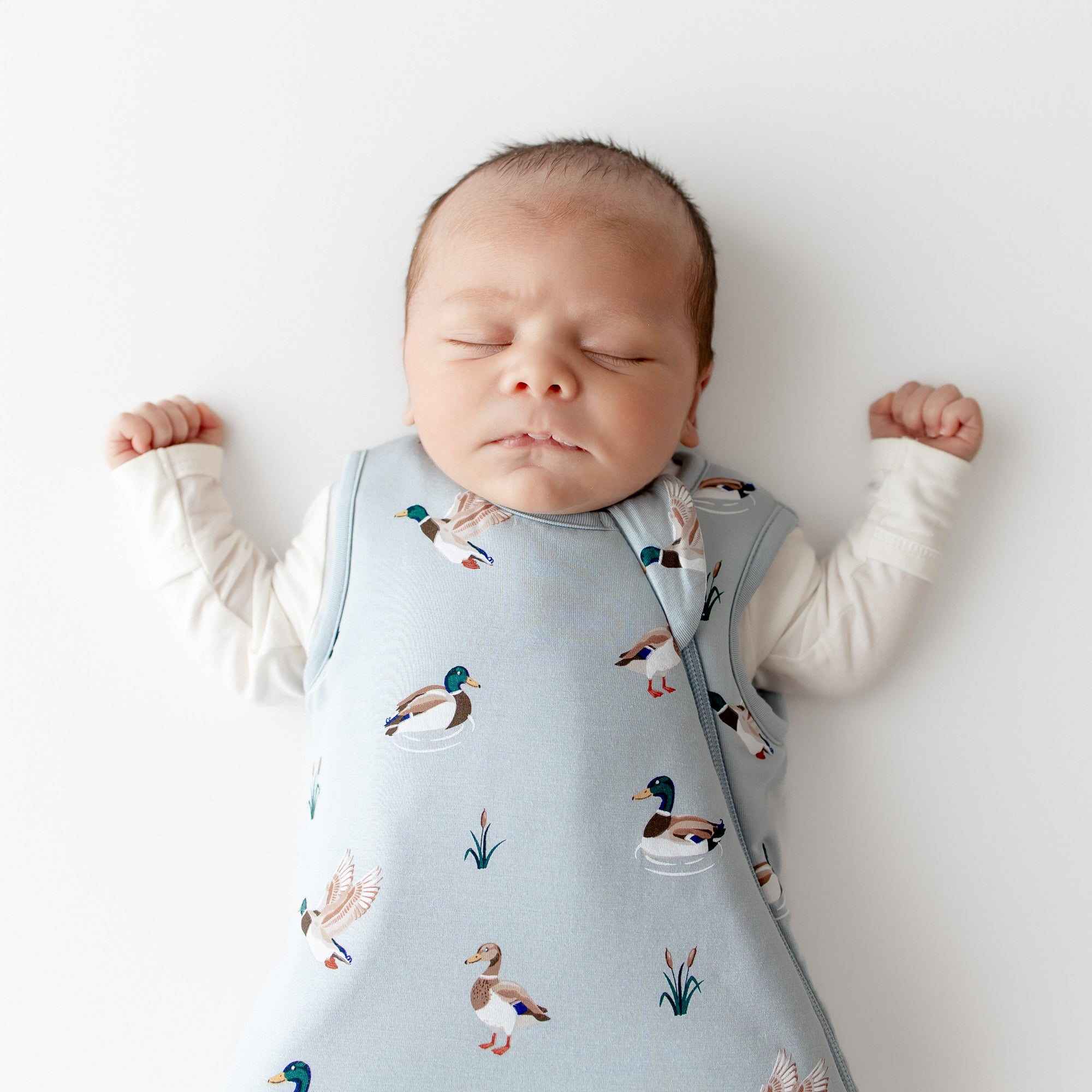 Close up of sleeping newborn wearing the Sleep Bag in Mallard Duck 1.0 with a white romper on underneath