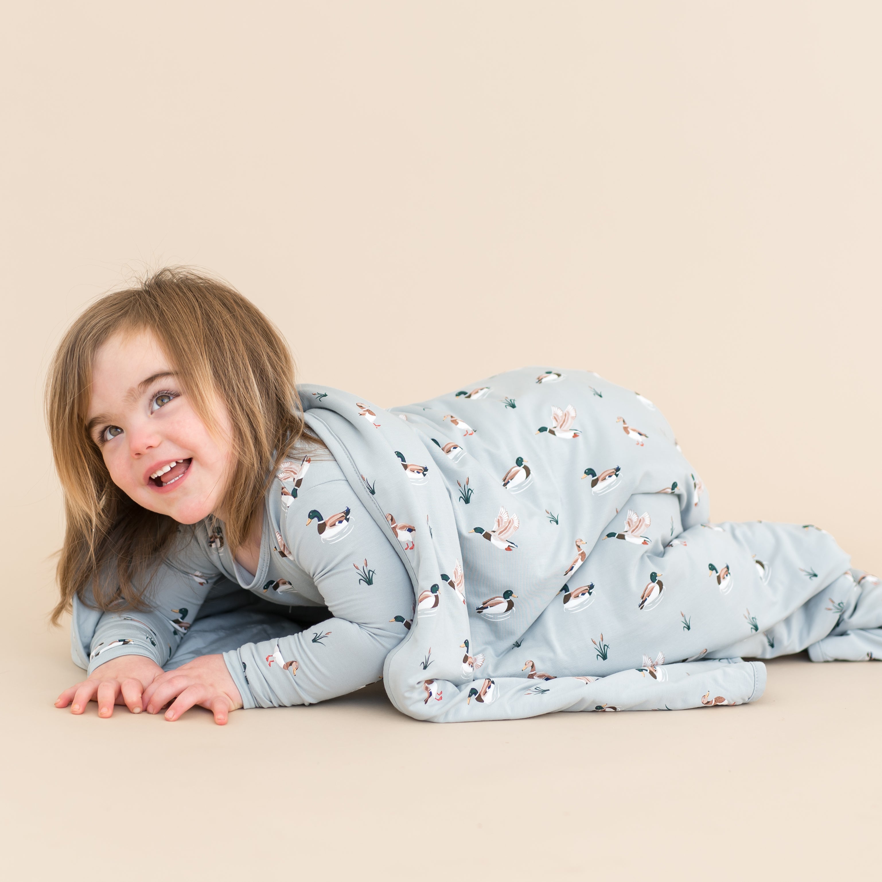 Young child laying on the ground with the Toddler Blanket in Mallard Duck 1.0 over top of them