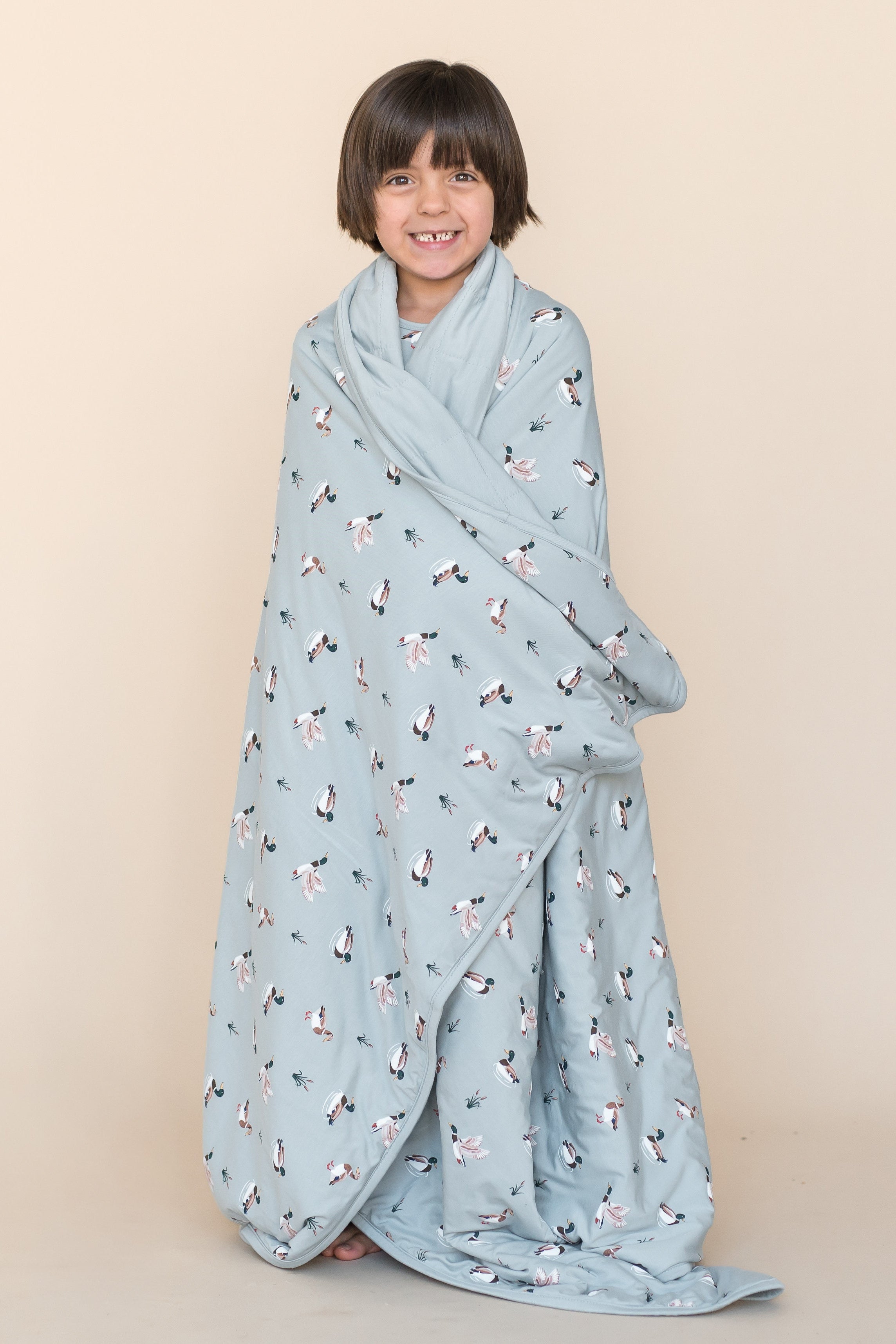 Young smiling boy standing wearing the Youth Blanket in Mallard Duck 1.0 around his shoulders