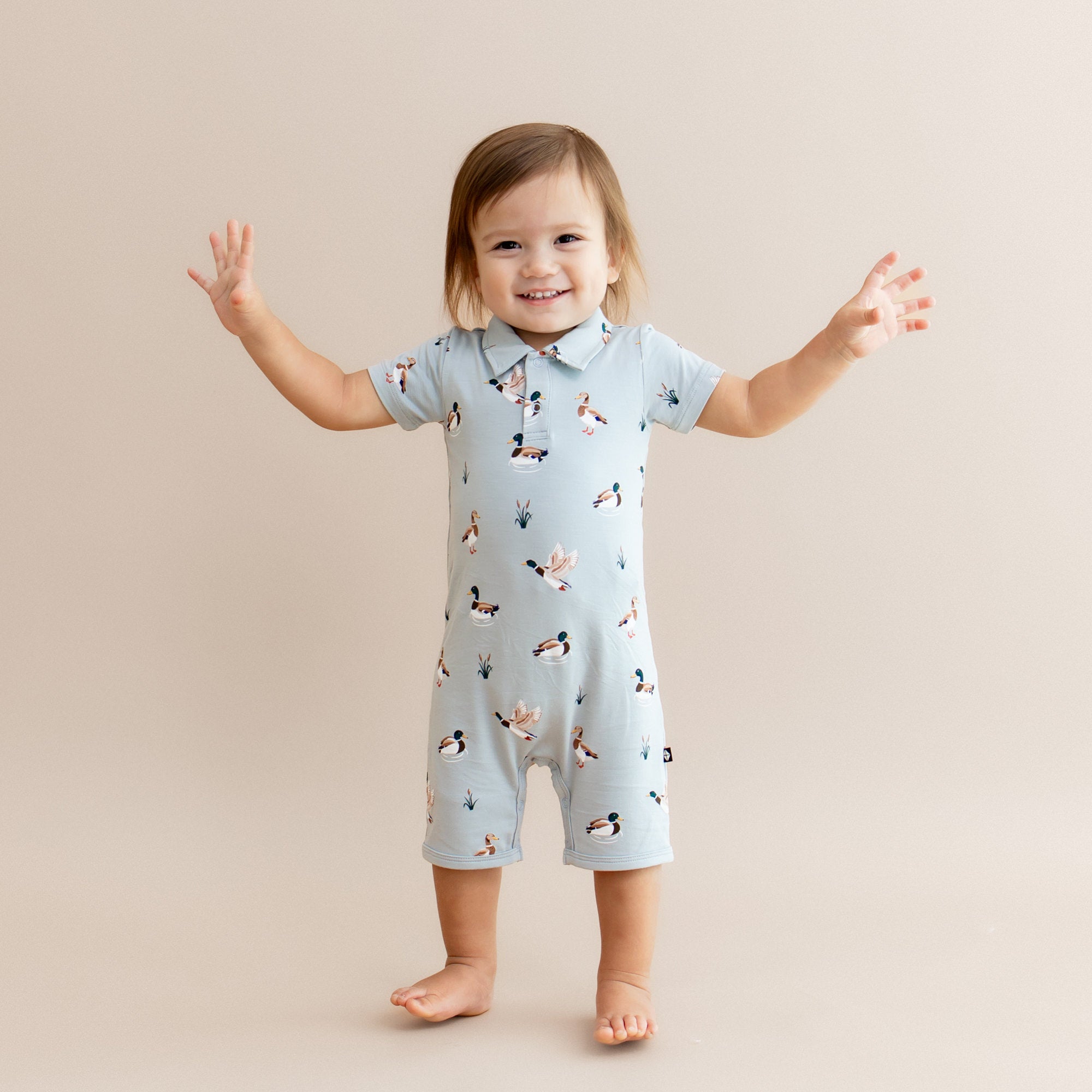 Young toddler standing with his arms out at the side wearing the Polo Shortall in Mallard Duck