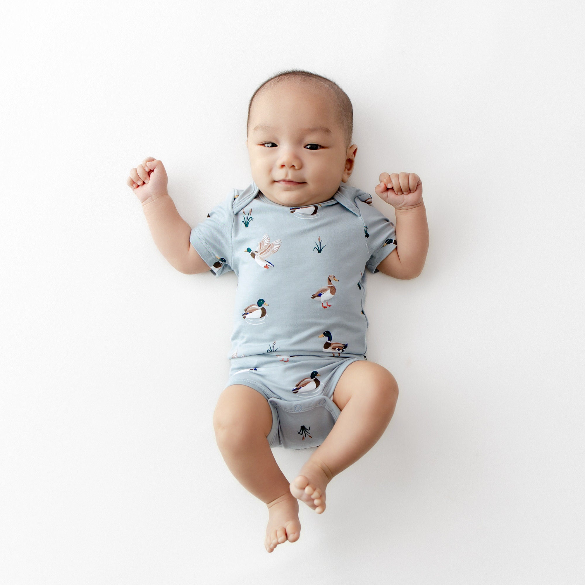 Newborn laying on a white surface wearing the Bodysuit in Mallard Duck