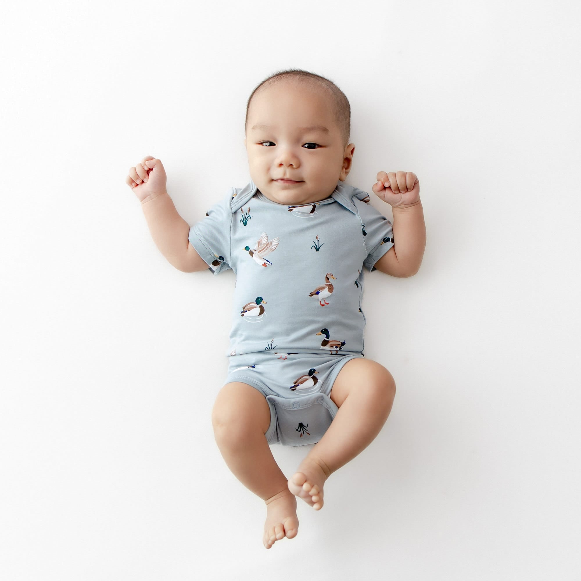Newborn laying on a white surface wearing the Bodysuit in Mallard Duck