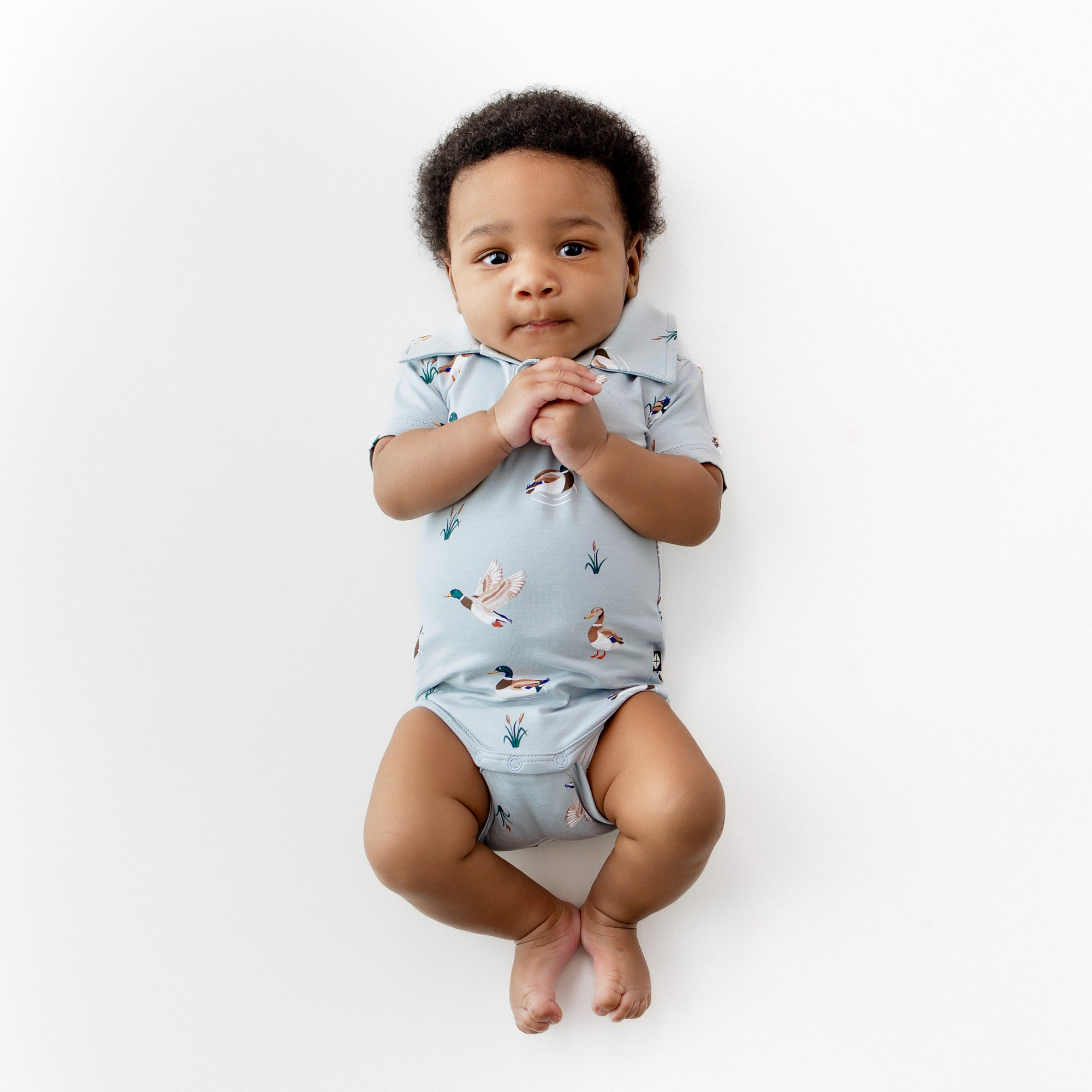 Infant laying on a white surface wearing the Polo Bodysuit in Mallard Duck