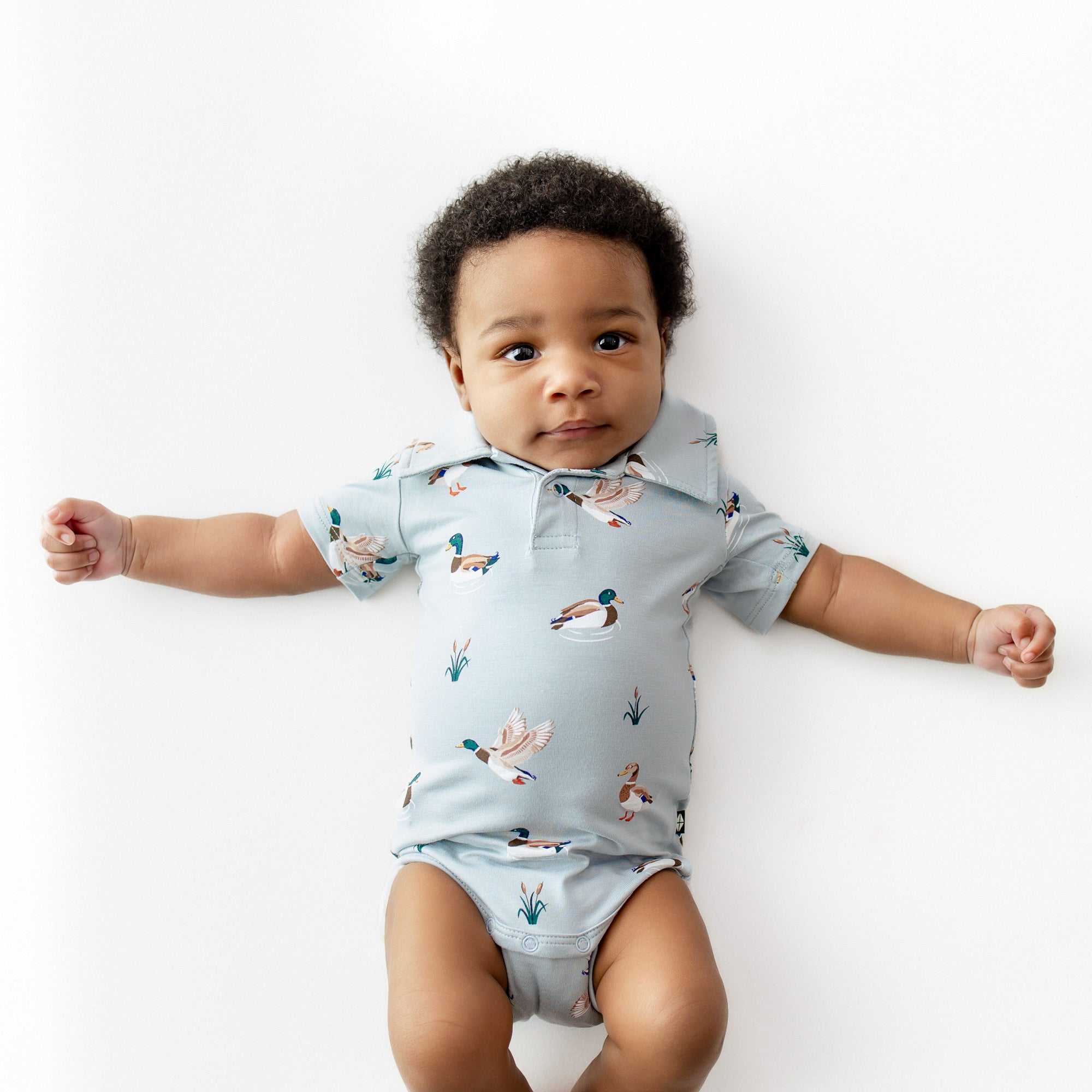 Infant wearing the Polo Bodysuit in Mallard Duck laying on a white surface
