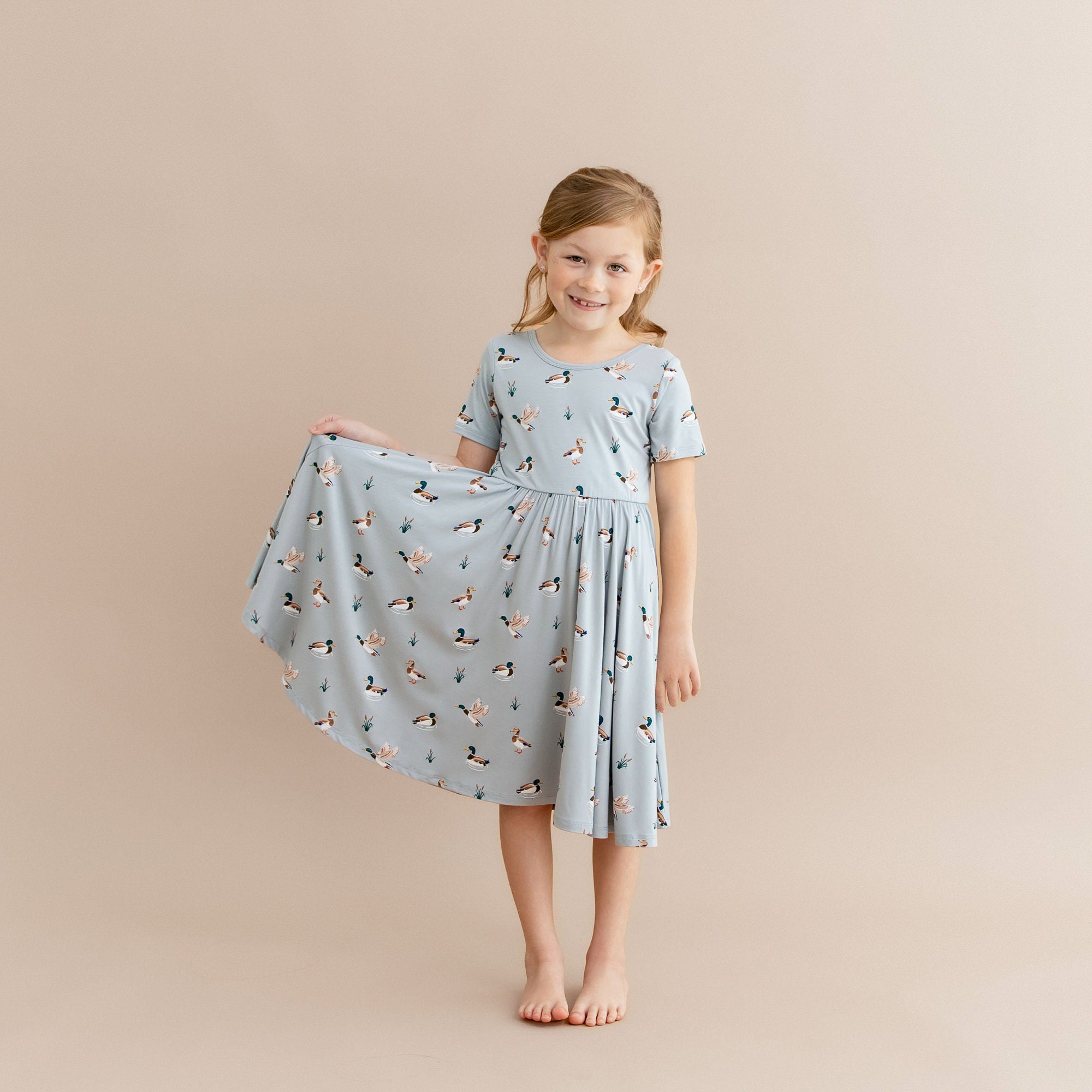 Young girl modeling the Twirl Dress in Mallard Duck holding out the skirt of the dress