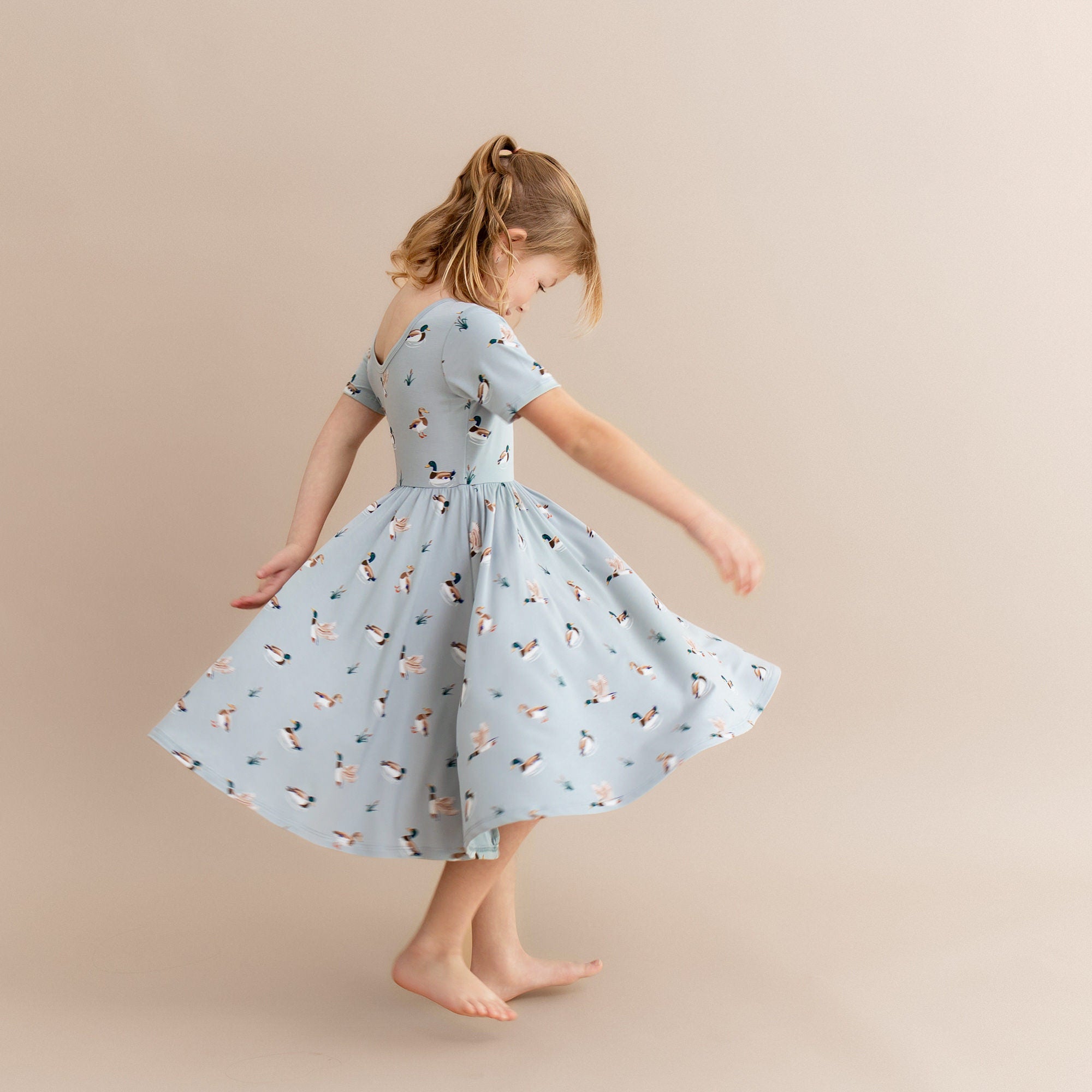 Young girl twirling wearing the Twirl Dress in Mallard Duck