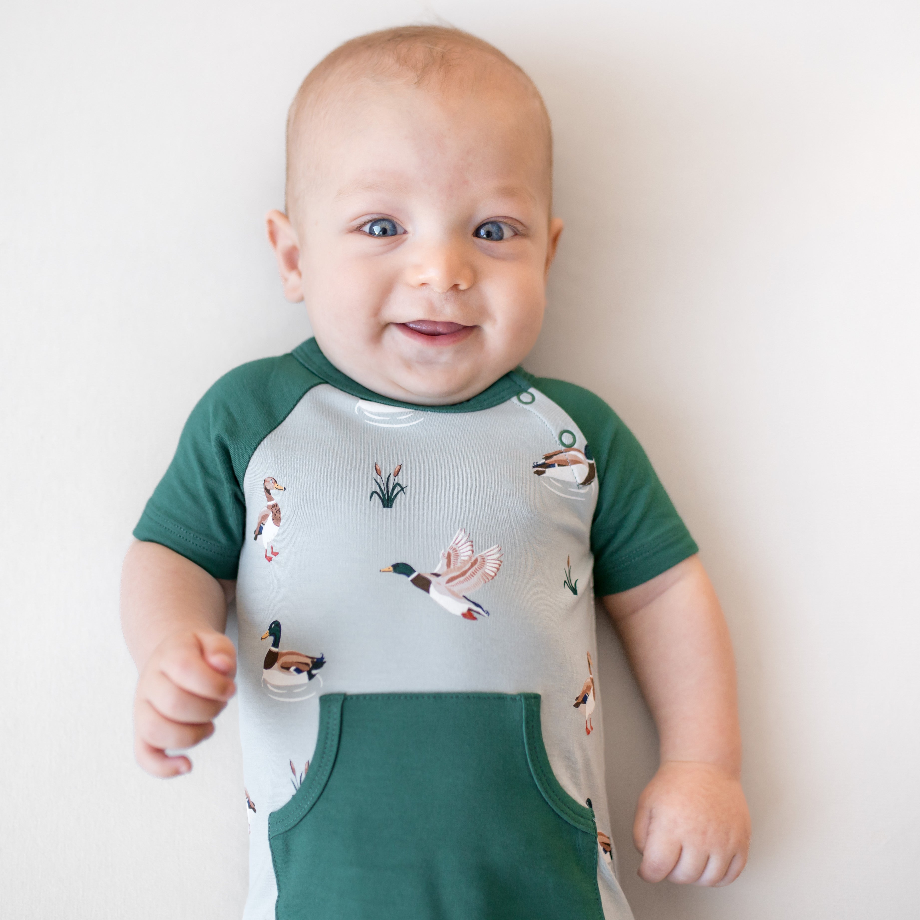 Close up of an infant wearing the Shortall in Mallard Duck showing the dark green trim and pocket