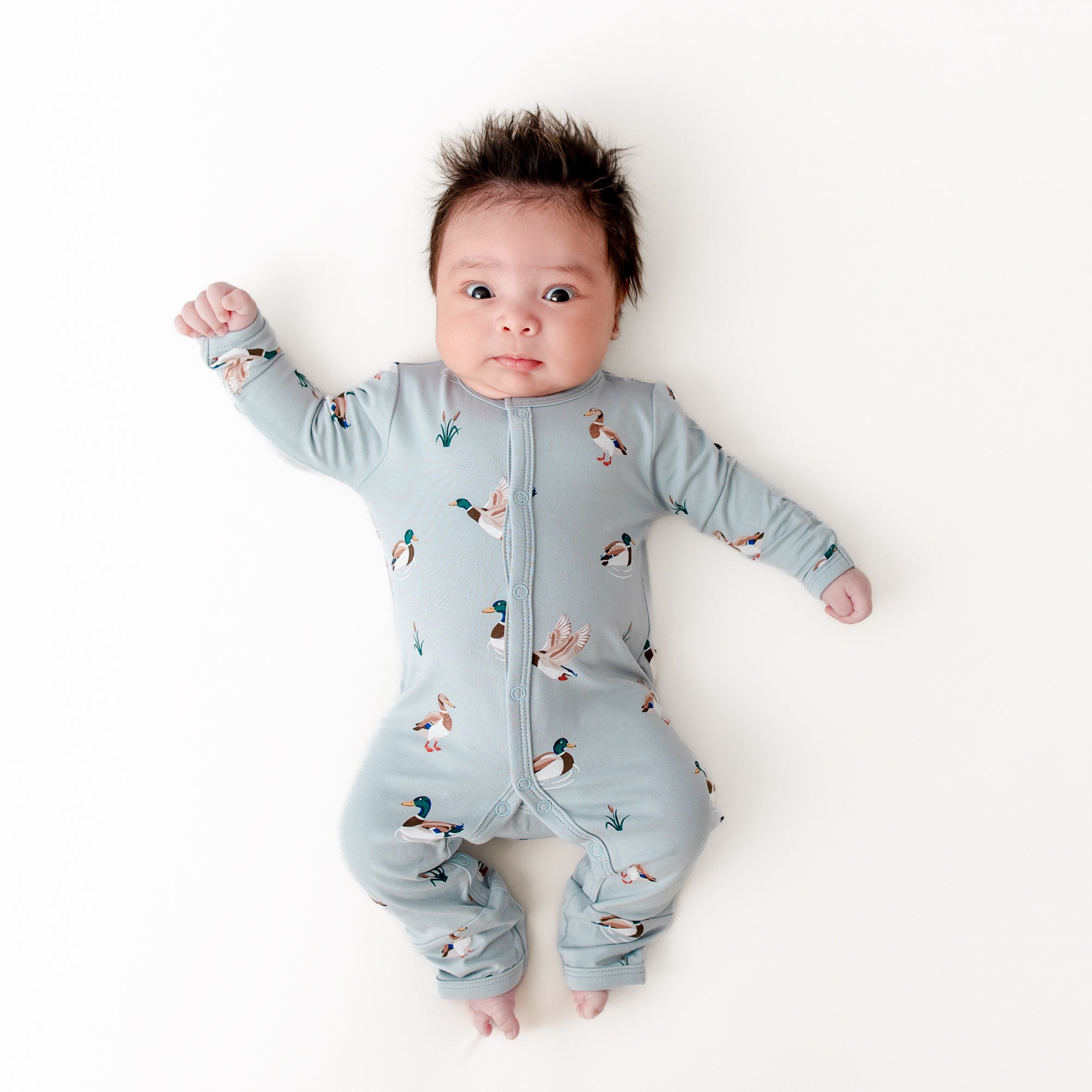 Newborn laying on a white surface wearing the Romper in Mallard Duck
