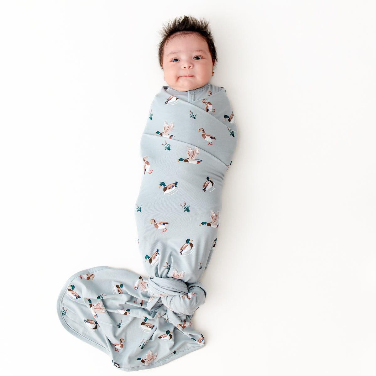 Newborn swaddled in the Swaddle Blanket in Mallard Duck laying on a white surface