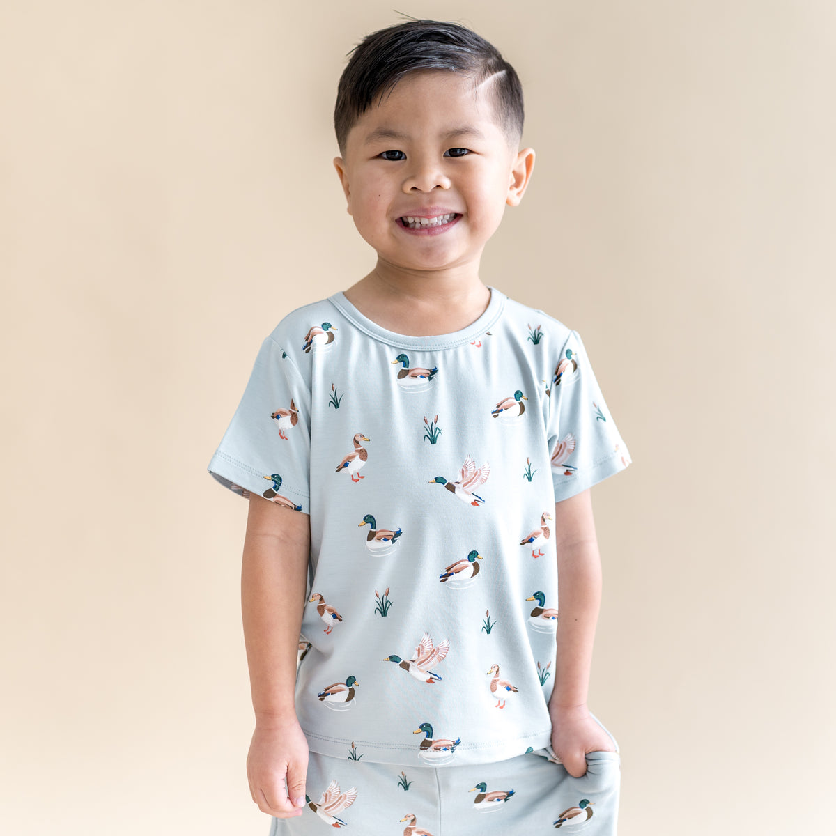 Smiling boy wearing the Toddler Basic Tee in Mallard Duck paired with matching drawstring shorts