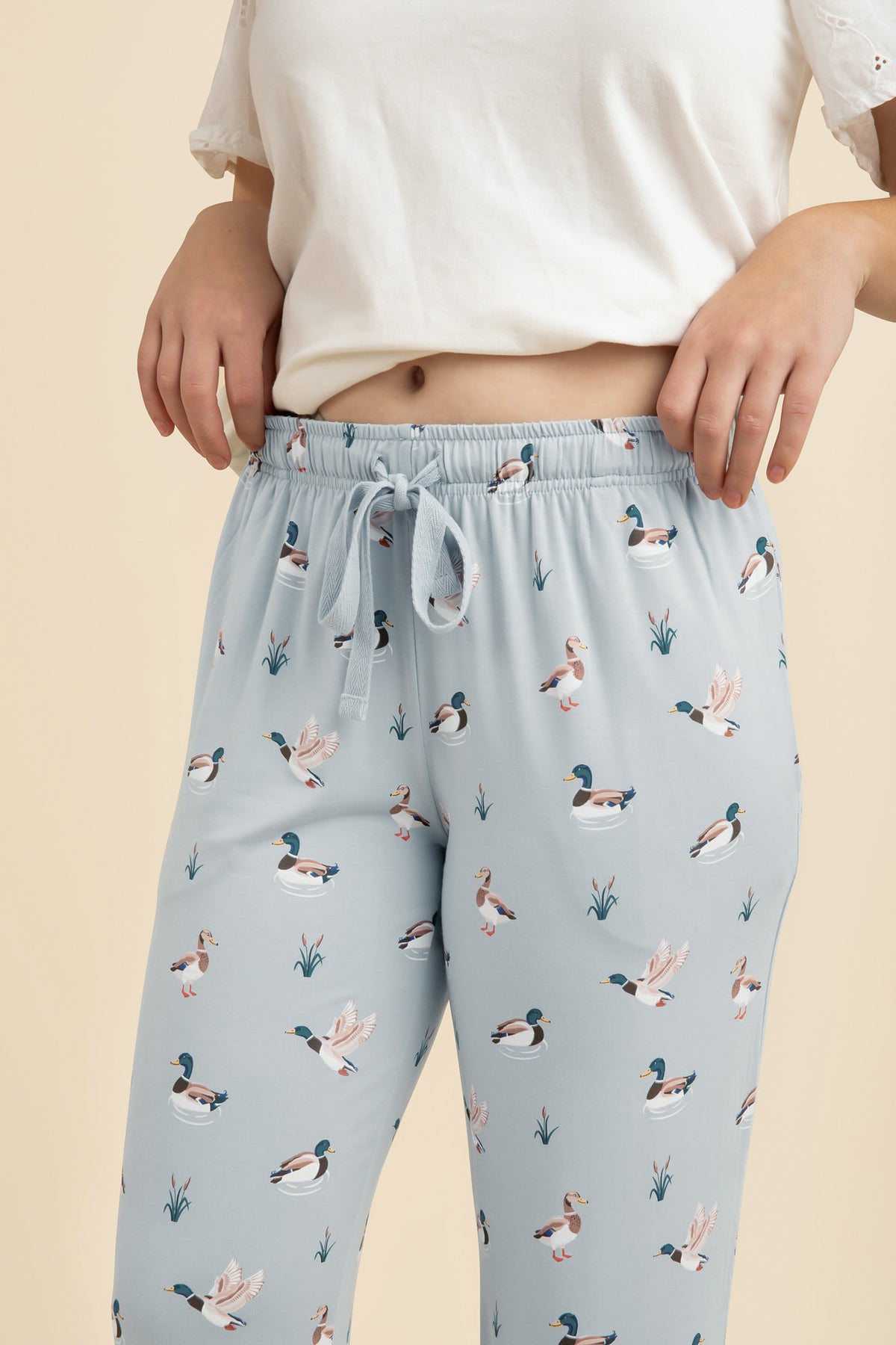 Light blue lounge pants with duck pattern worn by a person on a beige background