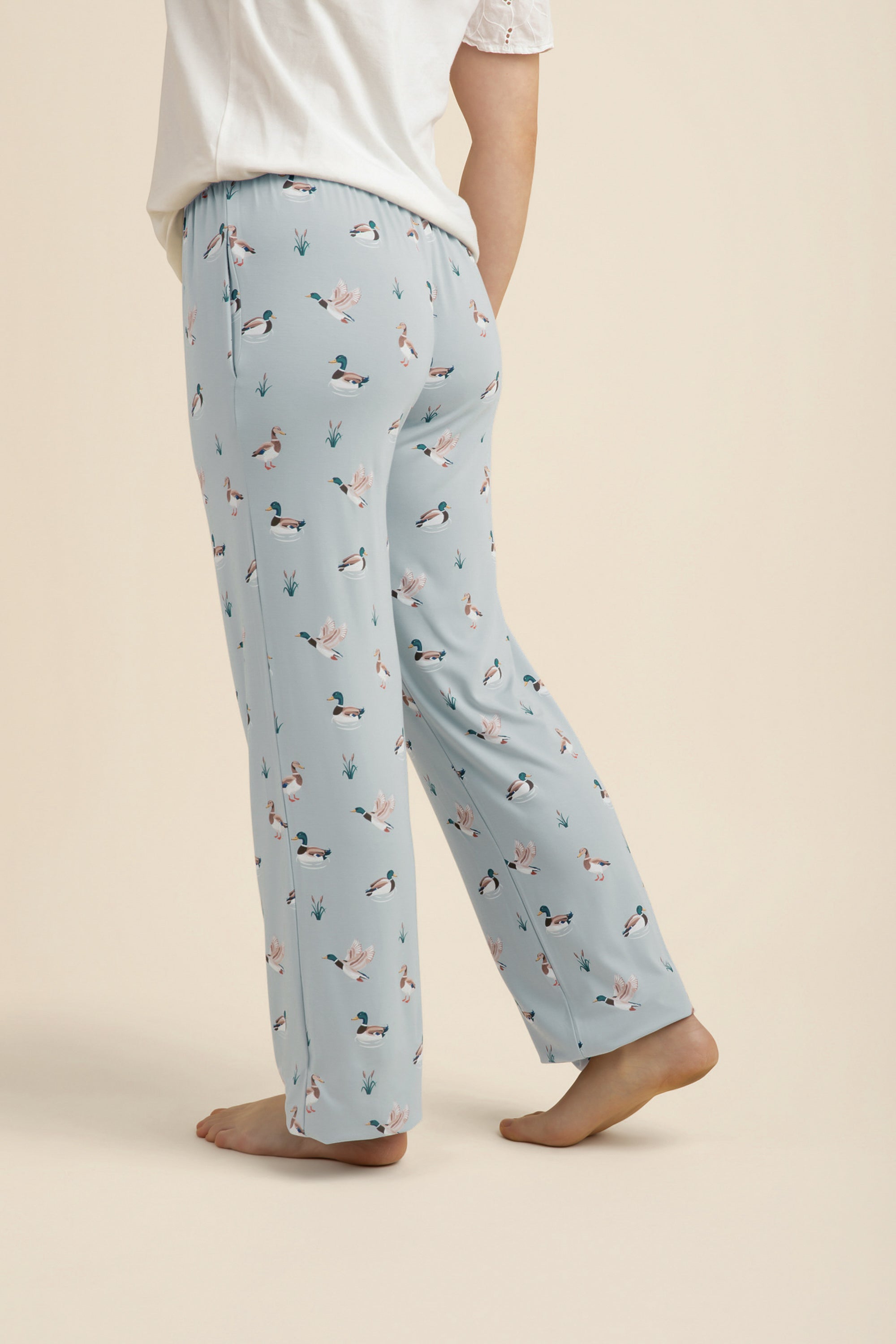 Light blue pajama pants with duck pattern worn by a person on a beige background