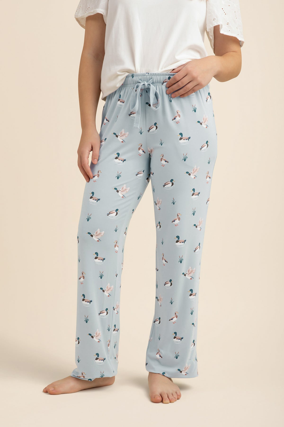 Light blue lounge pants with duck pattern worn by a person on a beige background