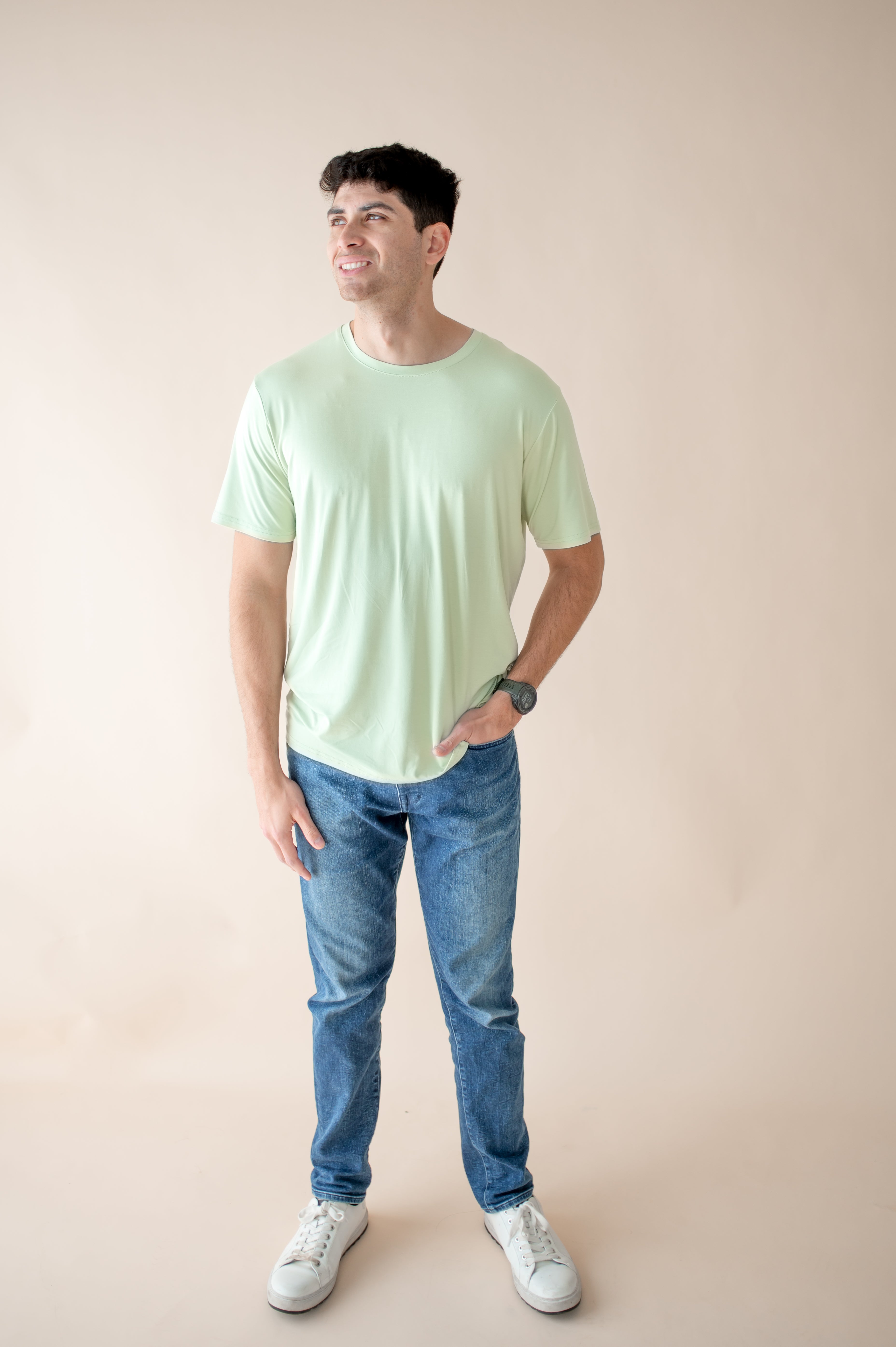 Male modeling the Men's Crew Neck Tee in Basil paired with medium wash jeans in front of a light neutral background