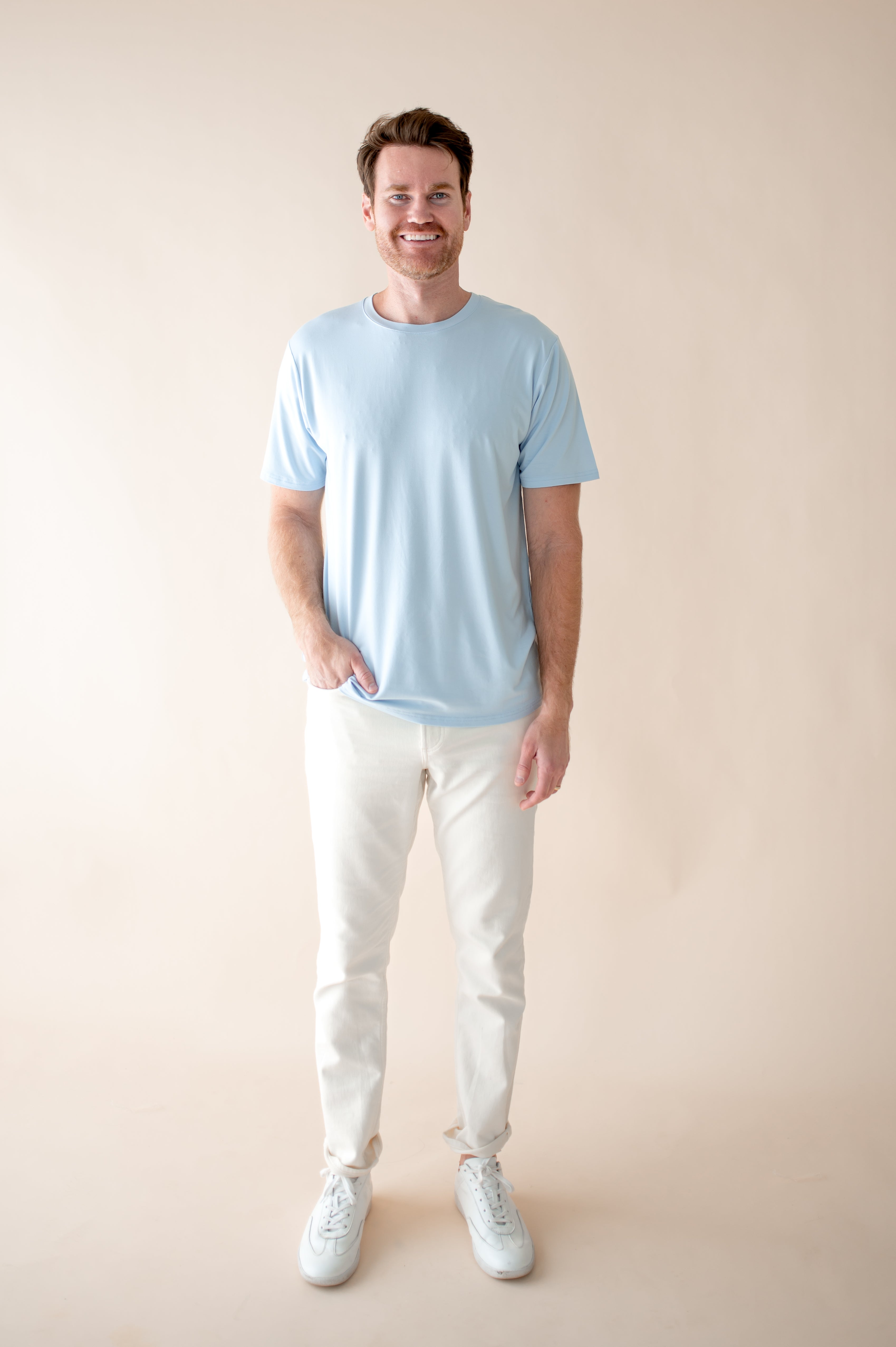 Smiling male model wearing the soft and breathable Men's Crew Neck Tee in Breeze paired with white pants with hand in pant pocket