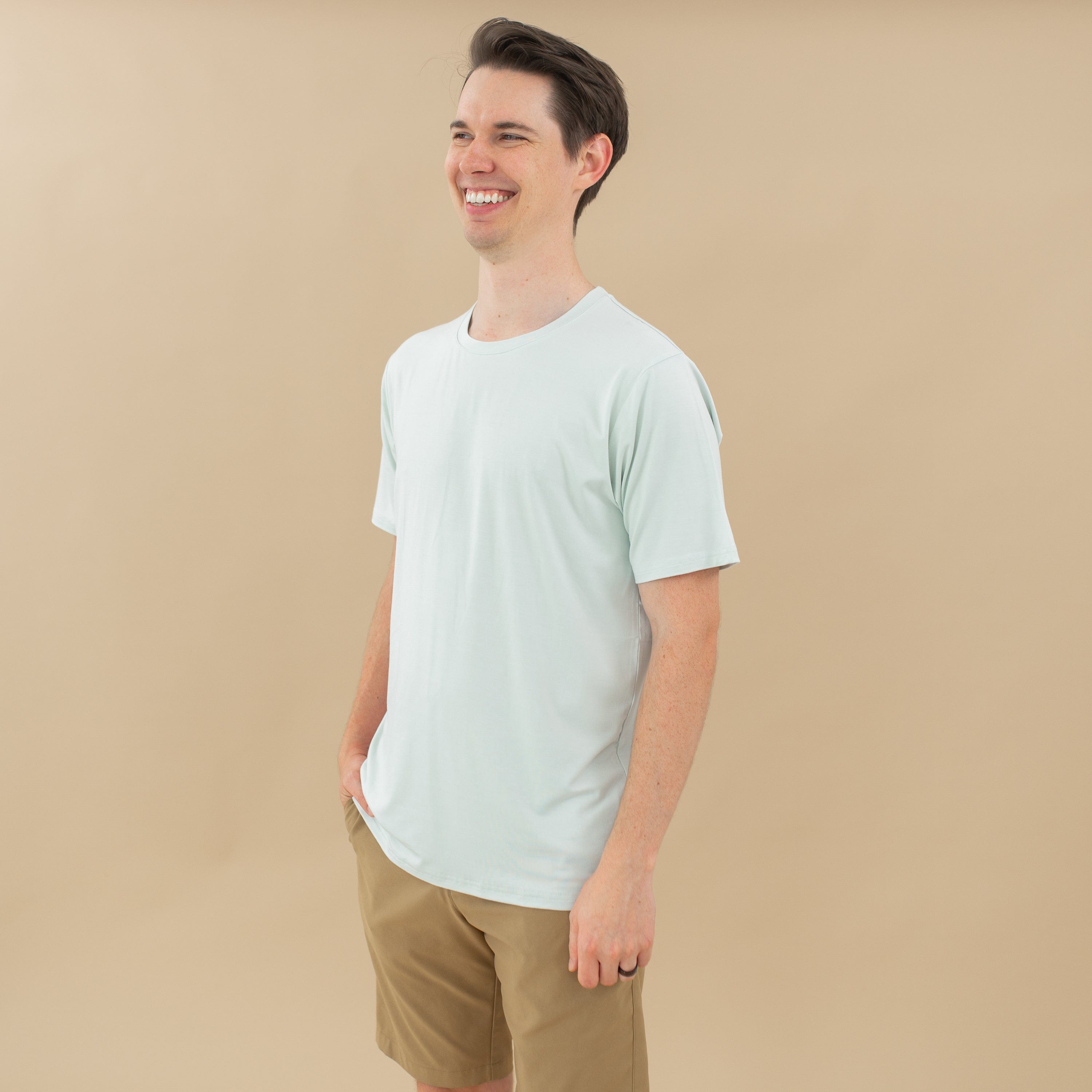 Smiling male model looking to the side wearing the Men's Crew Neck Tee in Dew and tan shorts