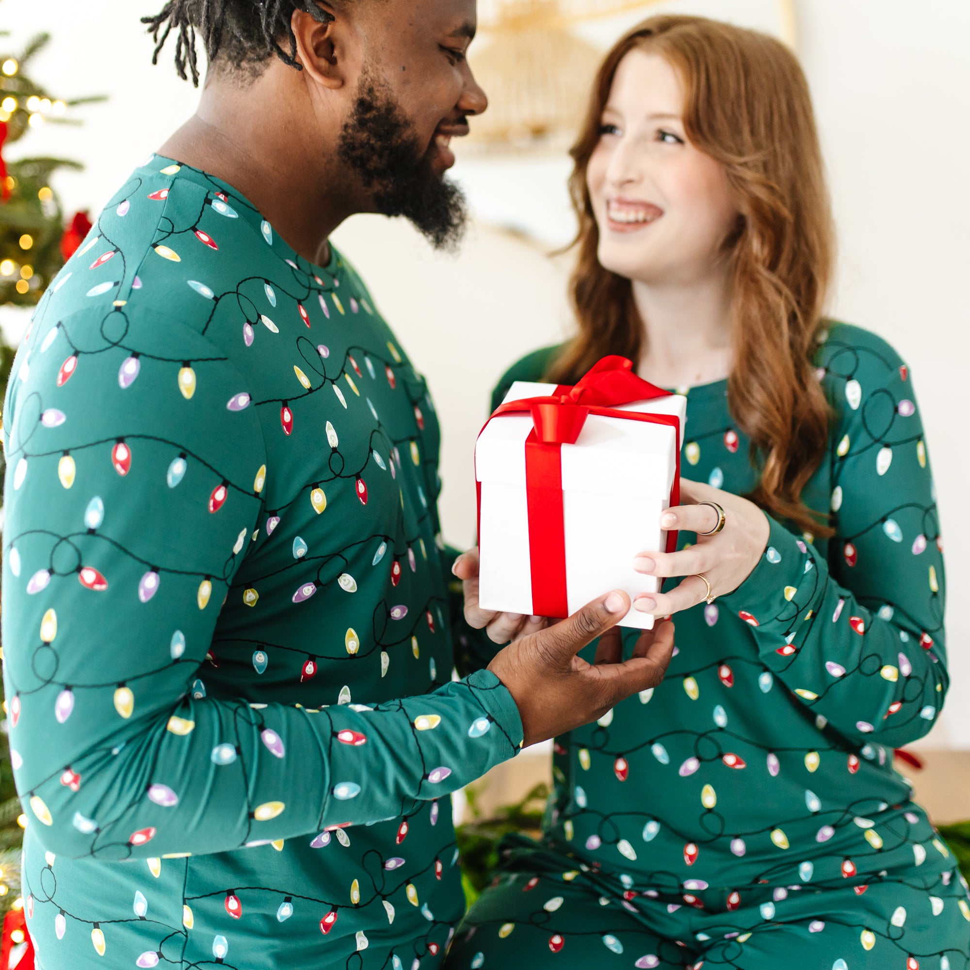 Couple each holding a gift box smiling and looking at one another both wearing the Men's and Women's Jogger Set in Merry and Brights