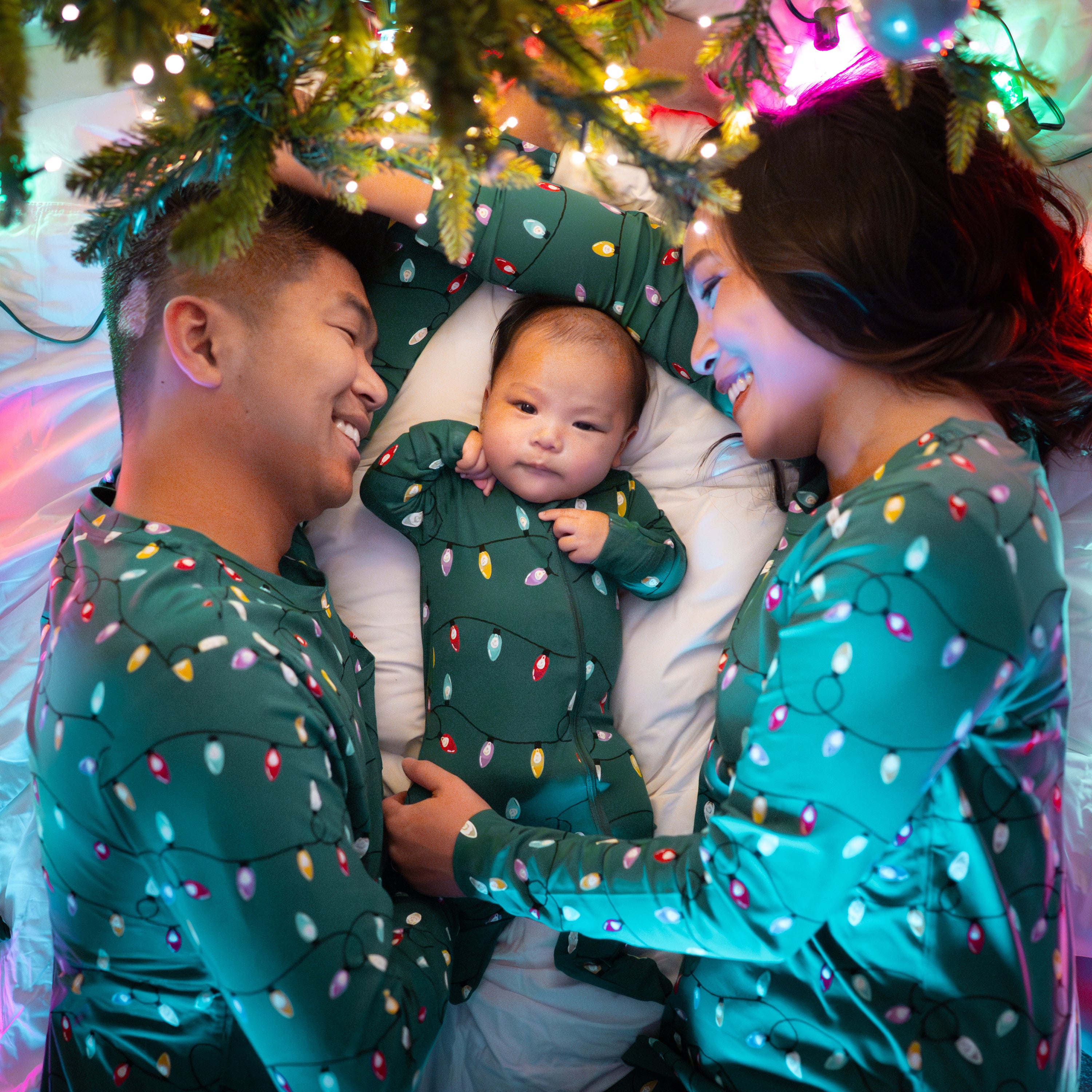 Family of three laying under a lit Christmas tree all matching in the holiday print Men's Jogger Set in Merry and Bright